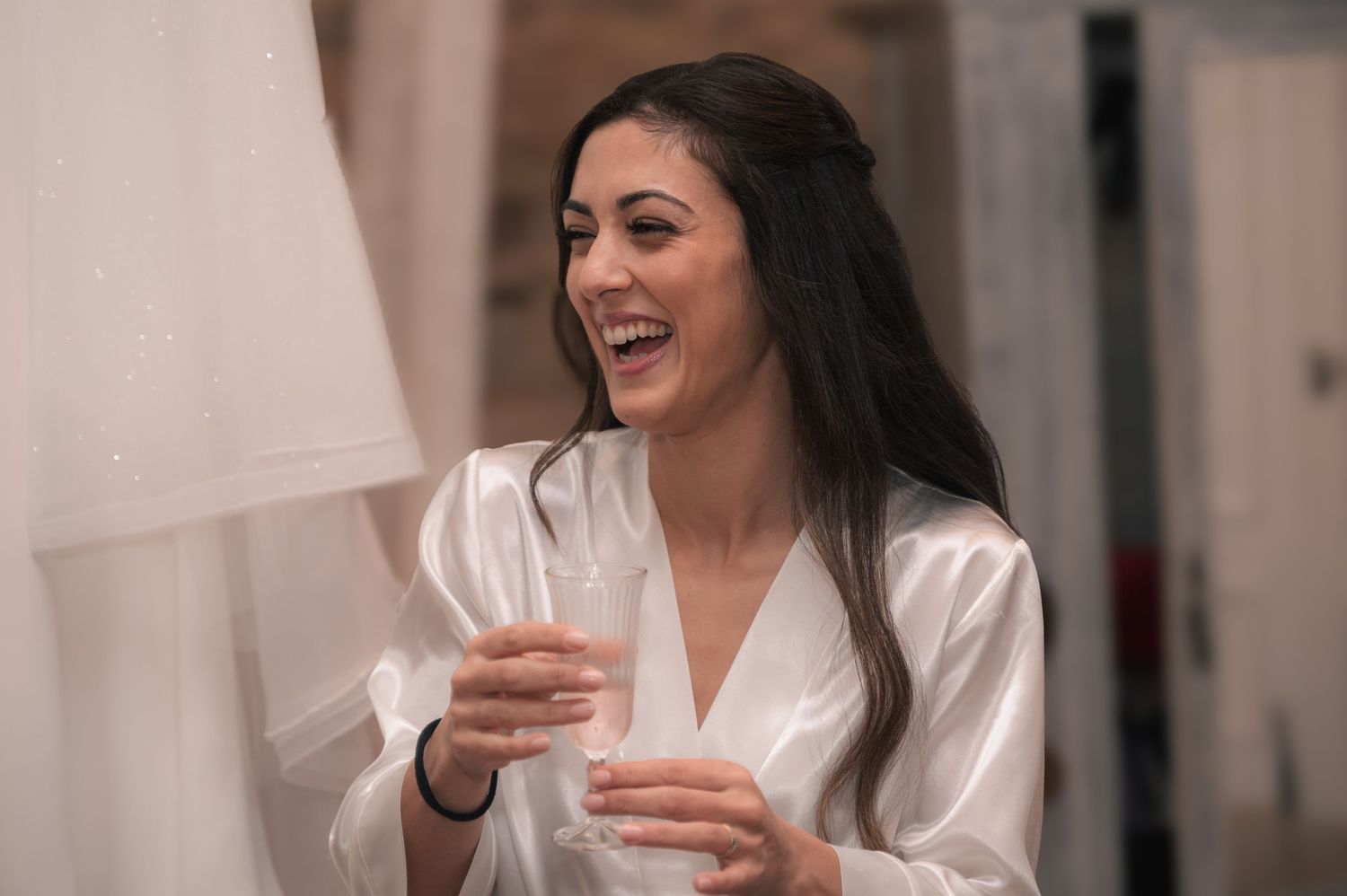 Two people laughing together while holding beverages against a rustic stone wall backdrop.