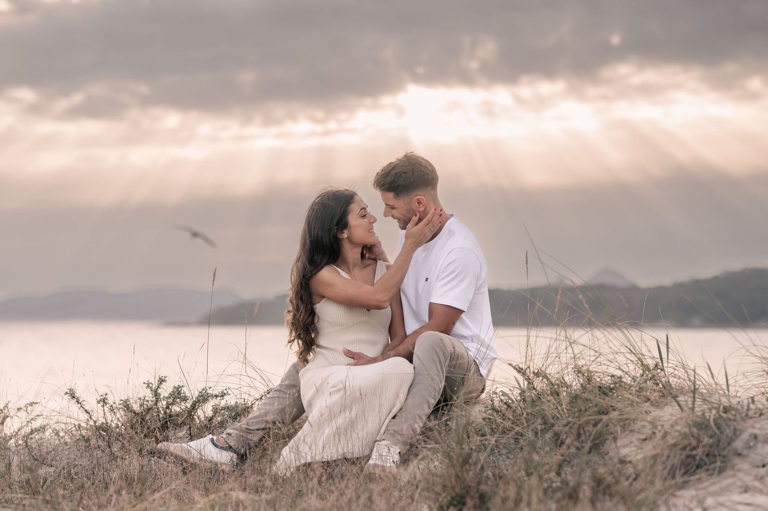 A couple in white clothing shares tender moments during a sunset photoshoot in nature.