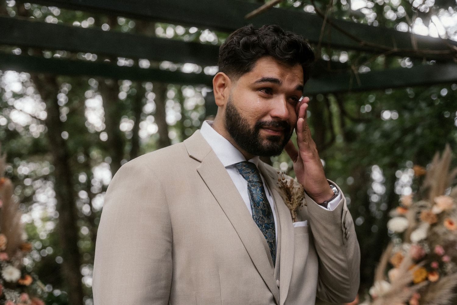 An emotional moment during an outdoor wedding ceremony under tall evergreen trees.