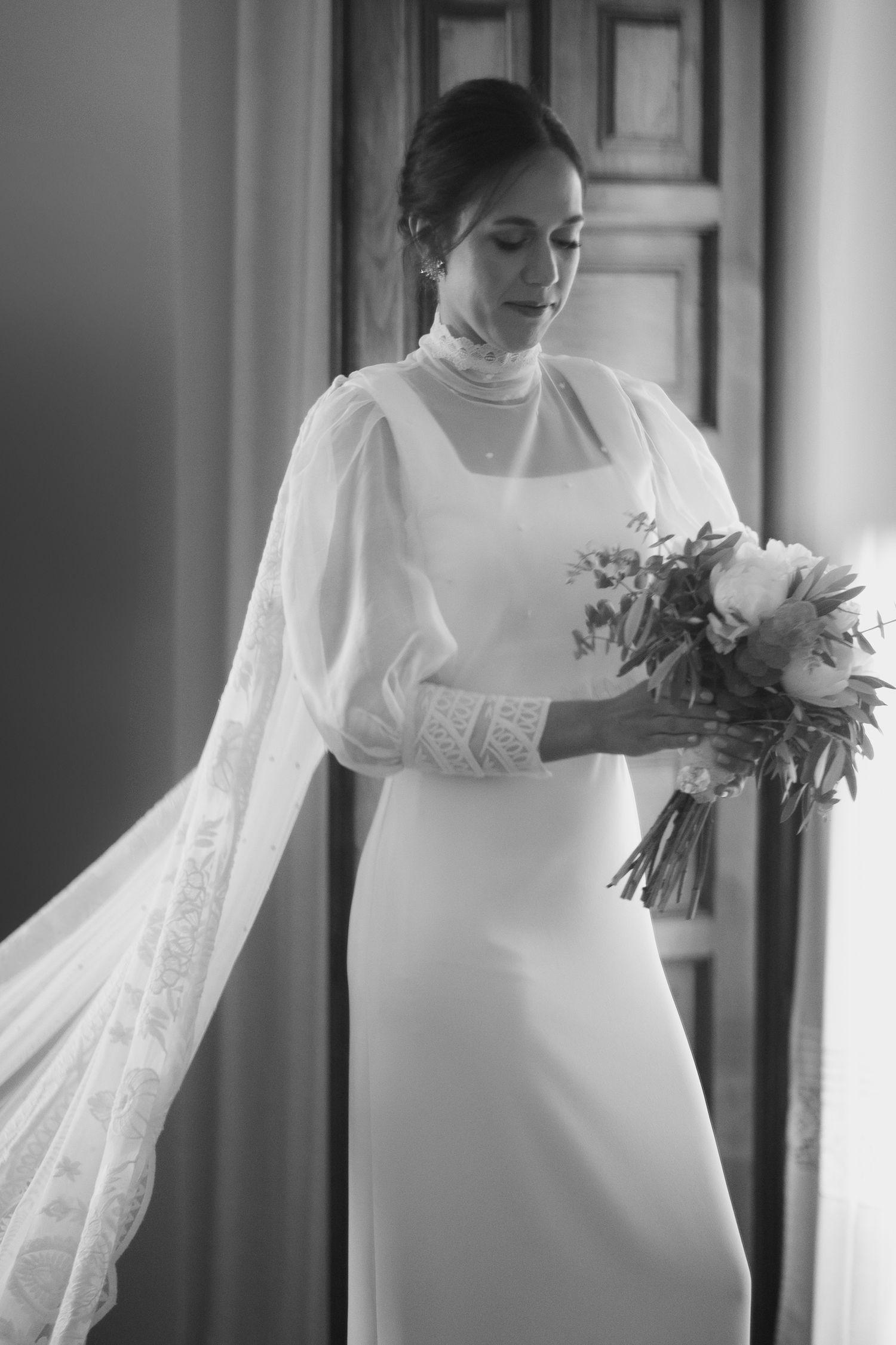 An elegant white wedding gown with long sleeves and lace details shown in classic black and white photography.