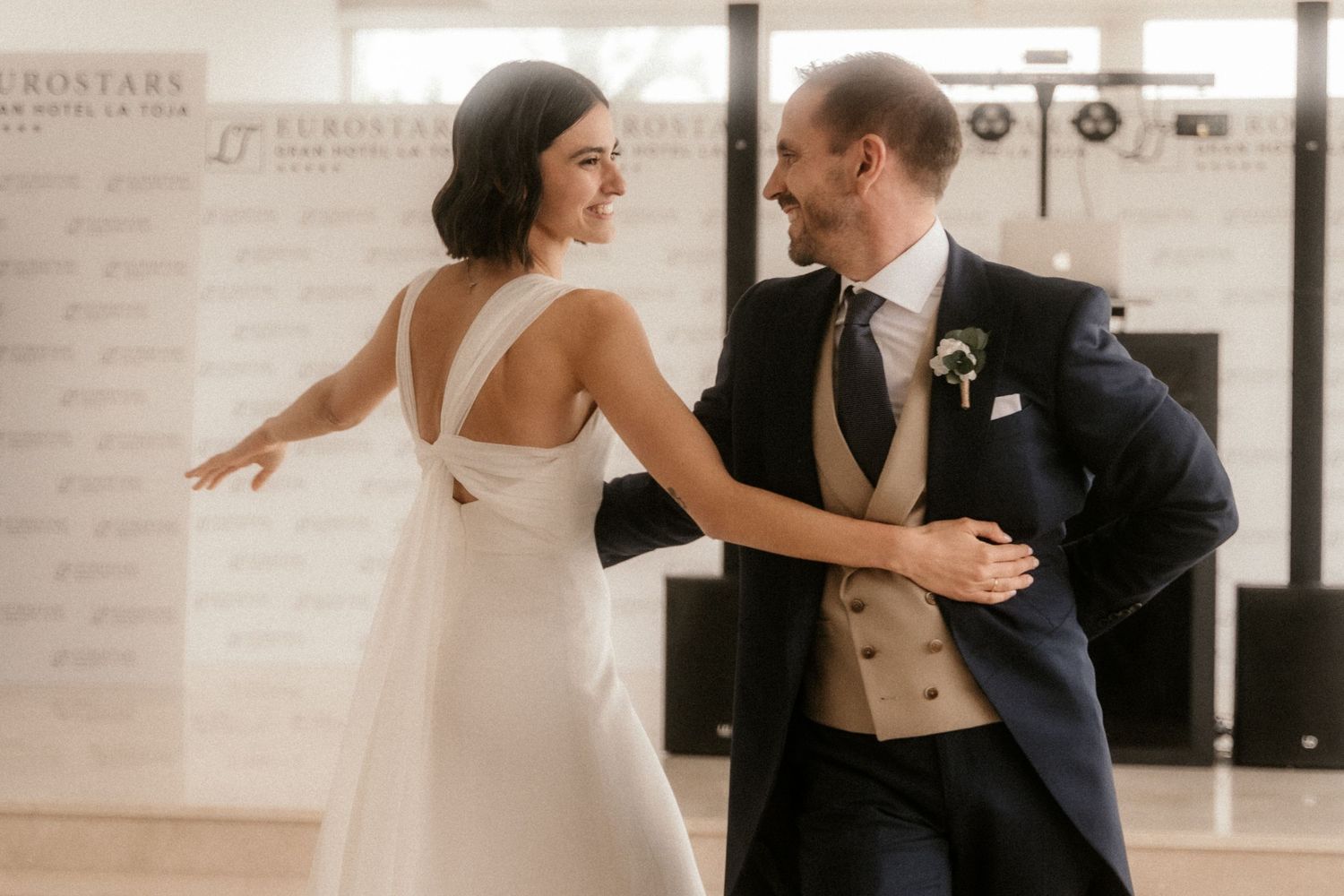 A couple shares their first dance at their wedding reception, with the bride in a sleek white gown and groom in navy suit.