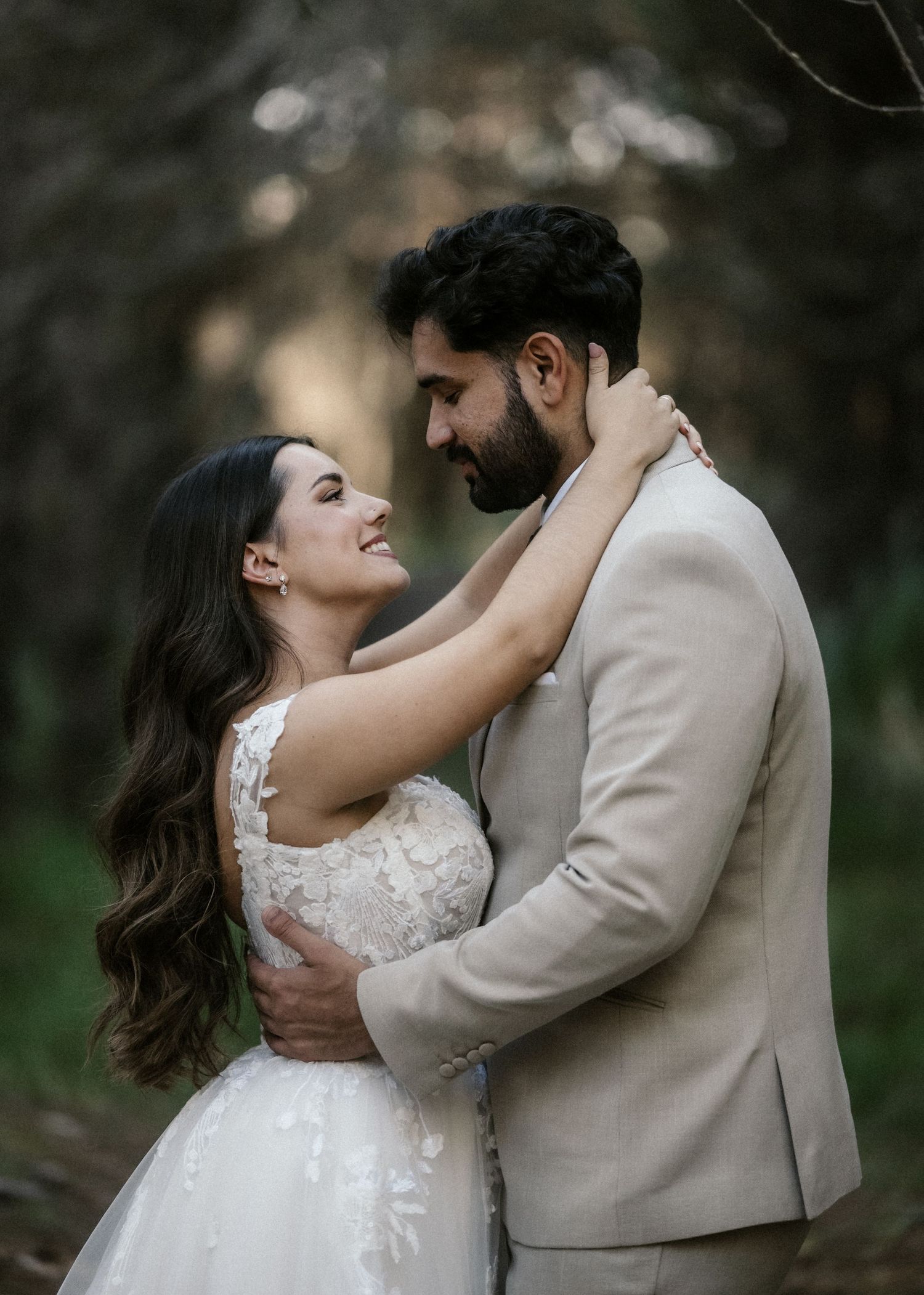 Newlyweds embrace tenderly outdoors with natural woodland backdrop and soft lighting.