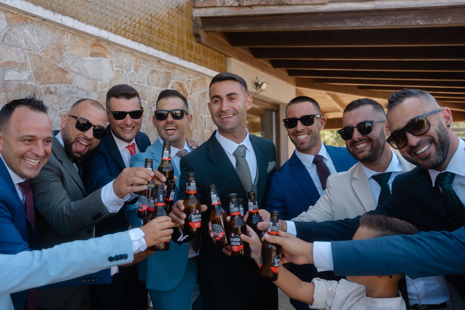 A group of formally dressed men in suits and sunglasses raise their glasses in a celebratory toast.