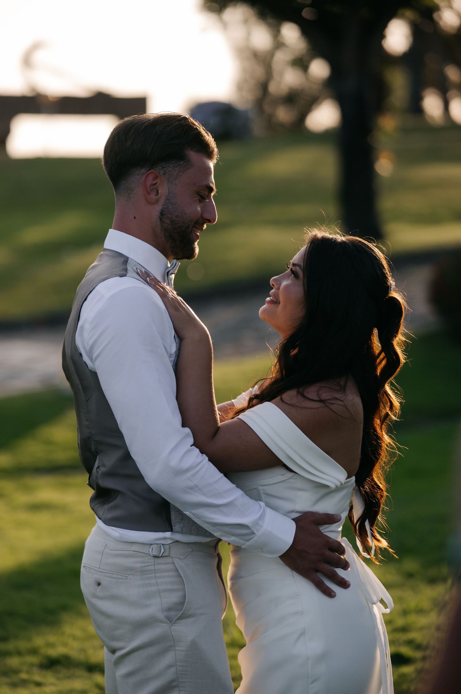 A romantic sunset wedding photo of a couple embracing outdoors on a grassy hill with golden light in the background.