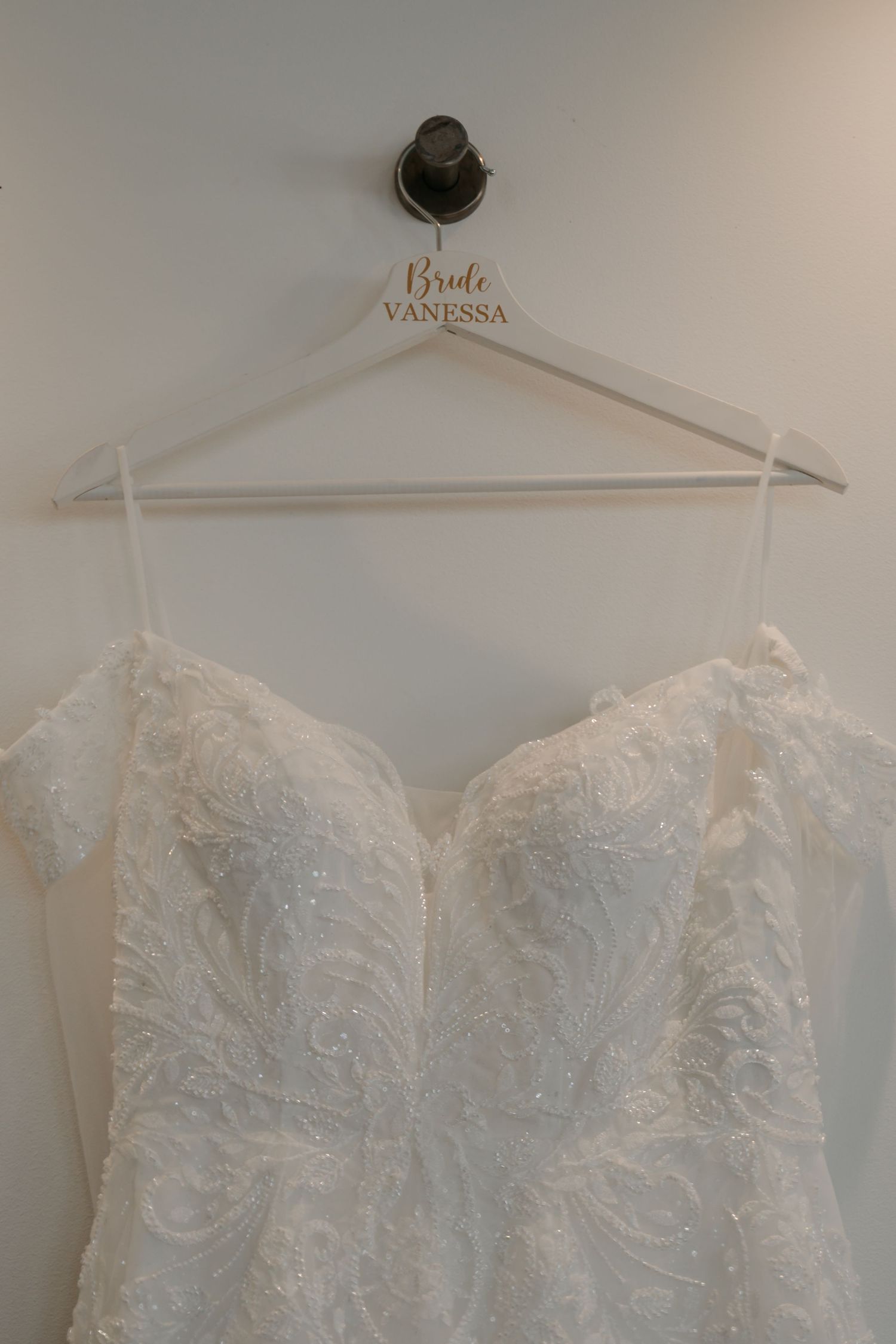 Elegant white lace wedding dress with intricate detailing hangs on a personalized bridal hanger.