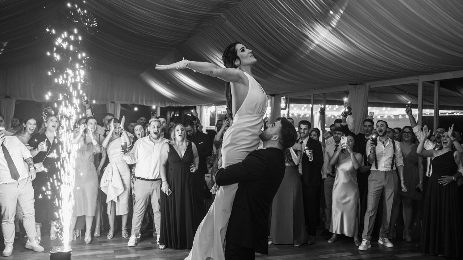 Black and white panoramic view of a wedding reception dance floor under an elegant tent canopy.