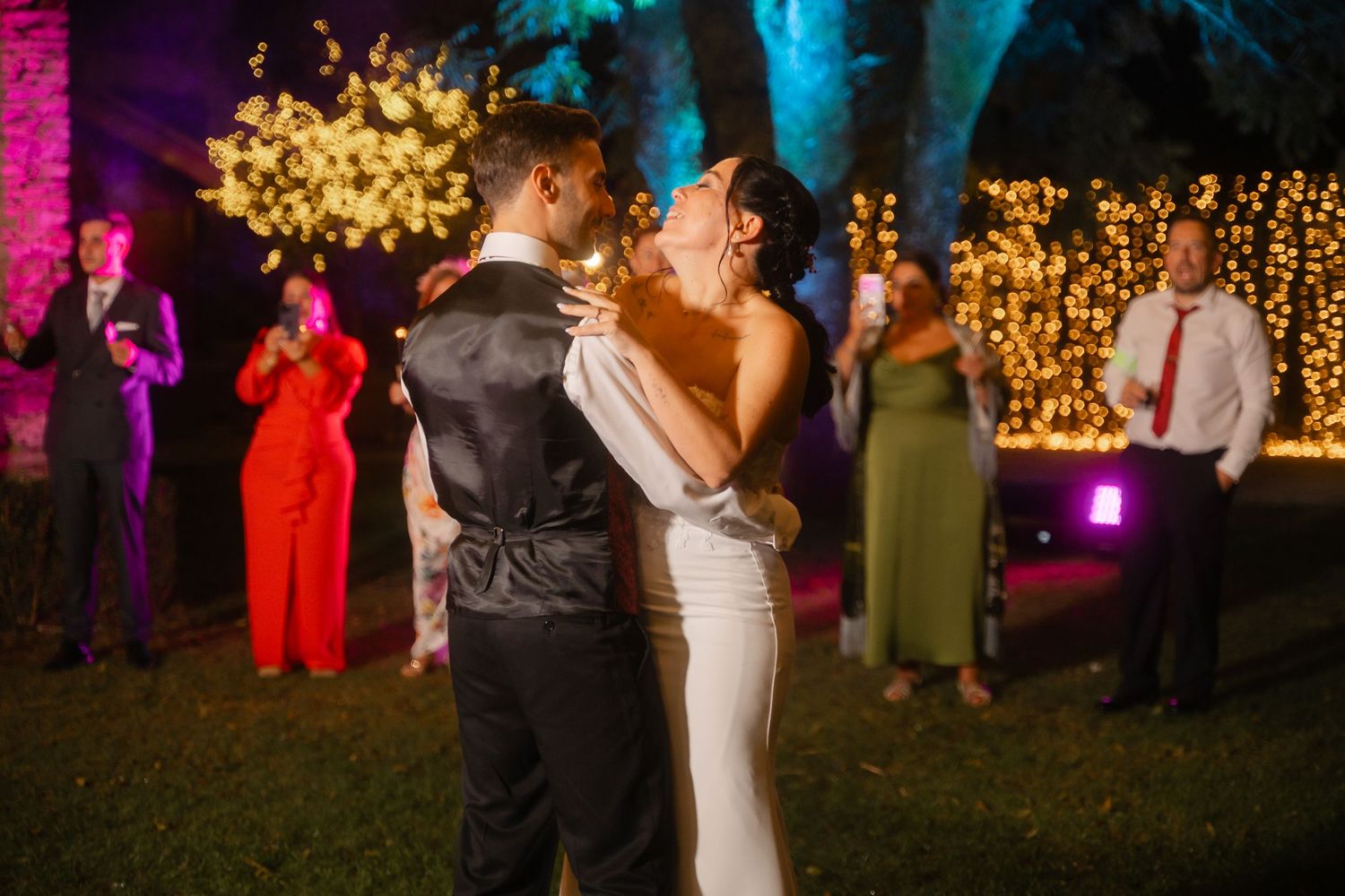 Couples dancing at a wedding reception with colorful pink and blue lighting creating a festive atmosphere.
