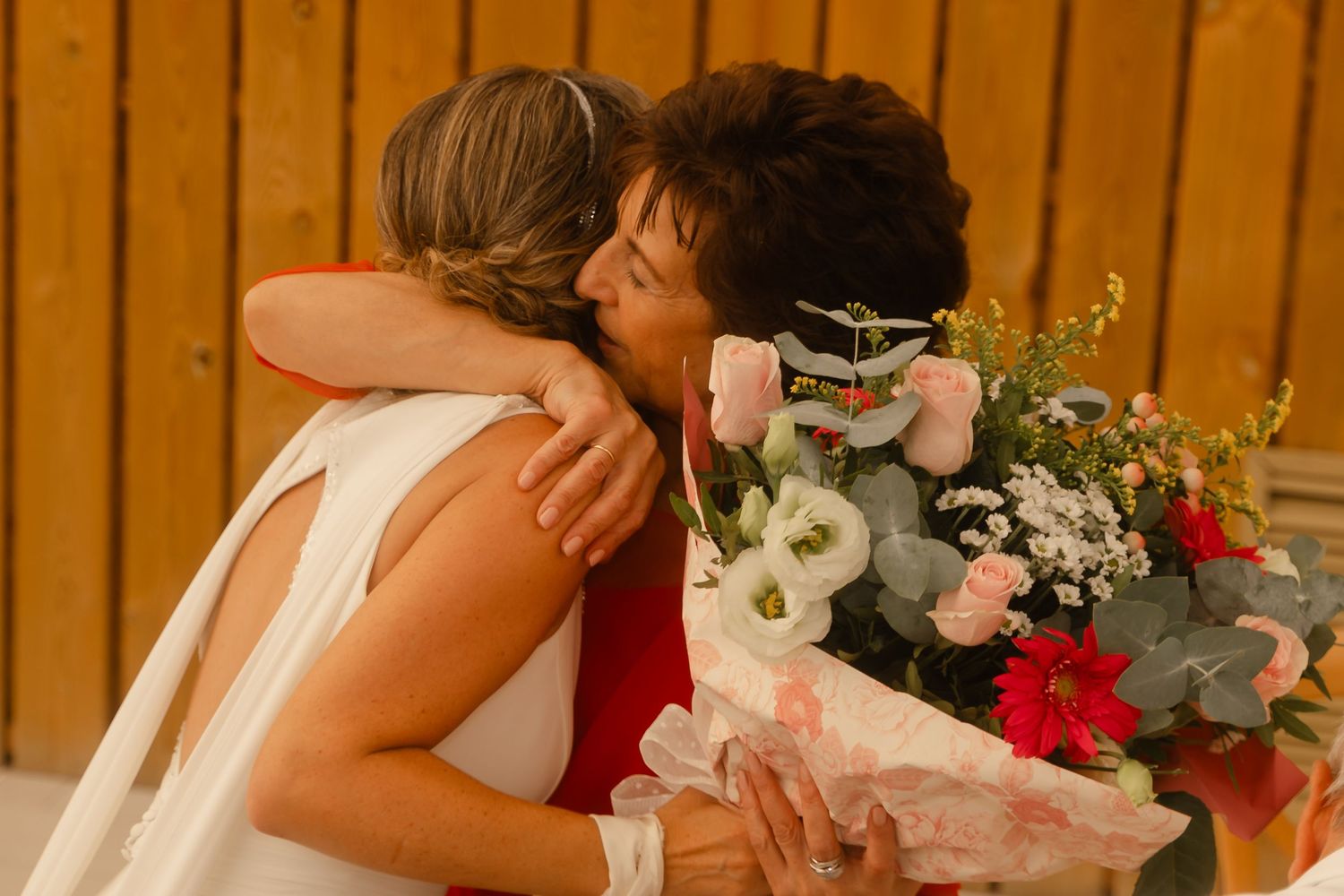 Floral centerpieces with red flowers and eucalyptus decorate wooden tables at a rustic wedding reception.