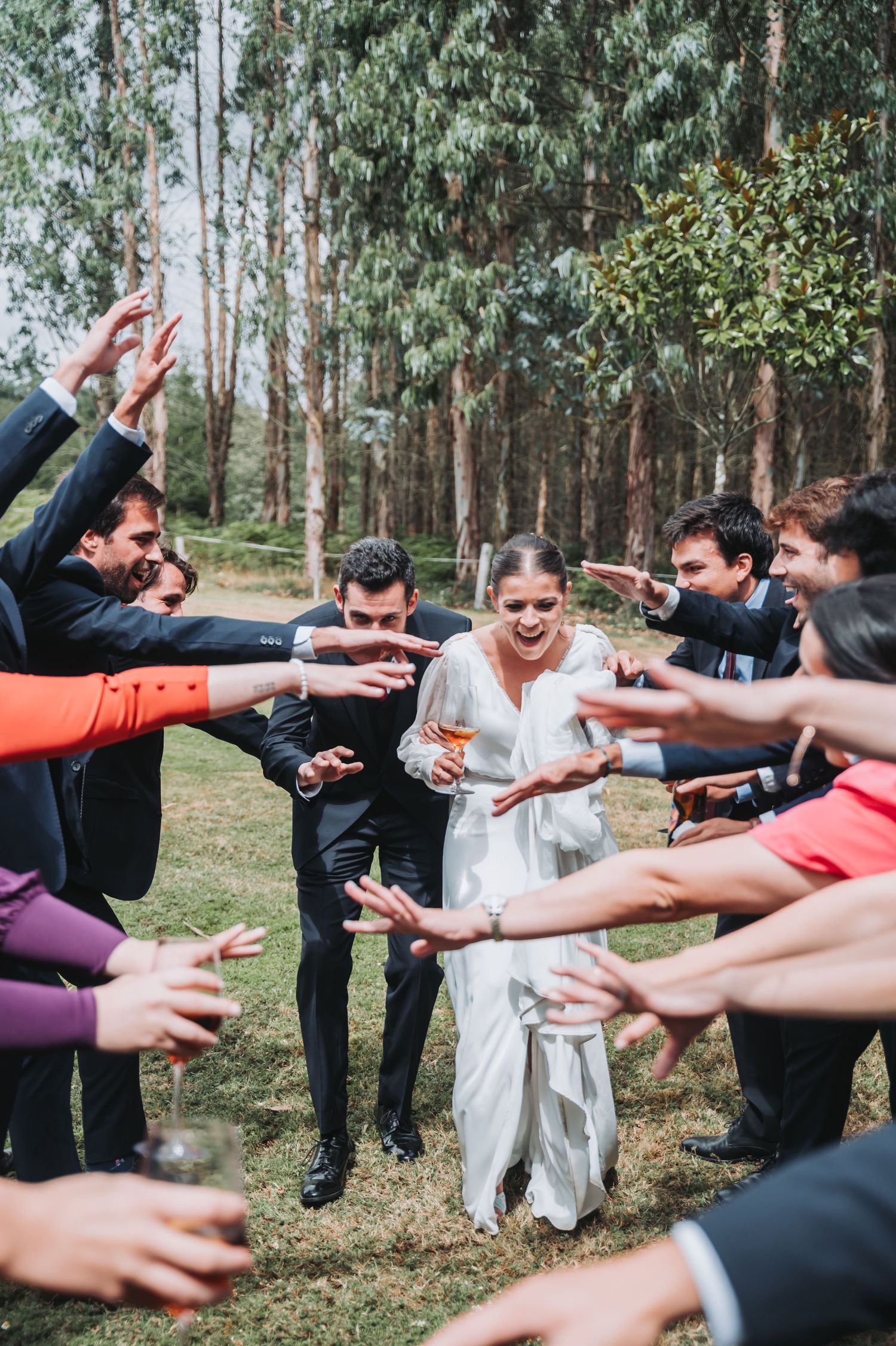 Wedding party forms a circle with outstretched arms in a eucalyptus forest, creating a joyful celebration moment.
