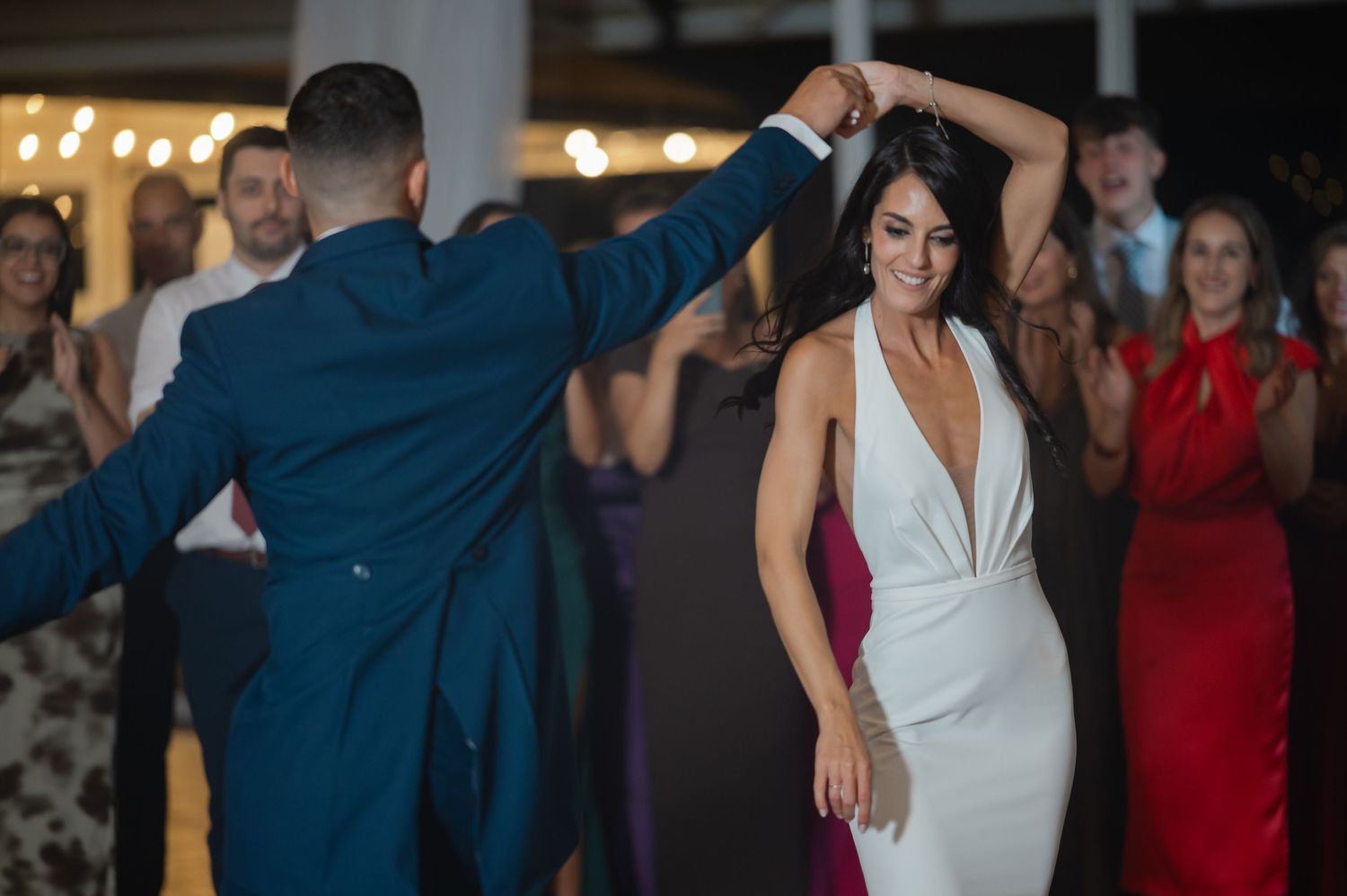 Couple dancing together at a wedding reception with guests watching and celebrating in the background.