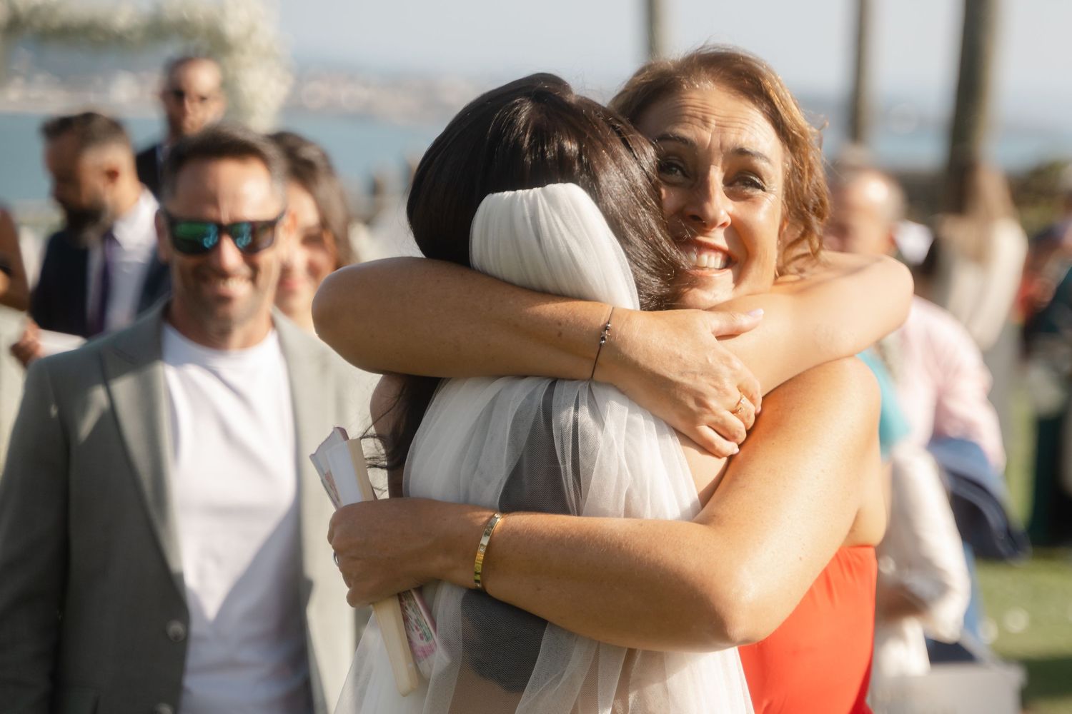 Happy wedding guests embrace and celebrate during an outdoor ceremony on a sunny day.