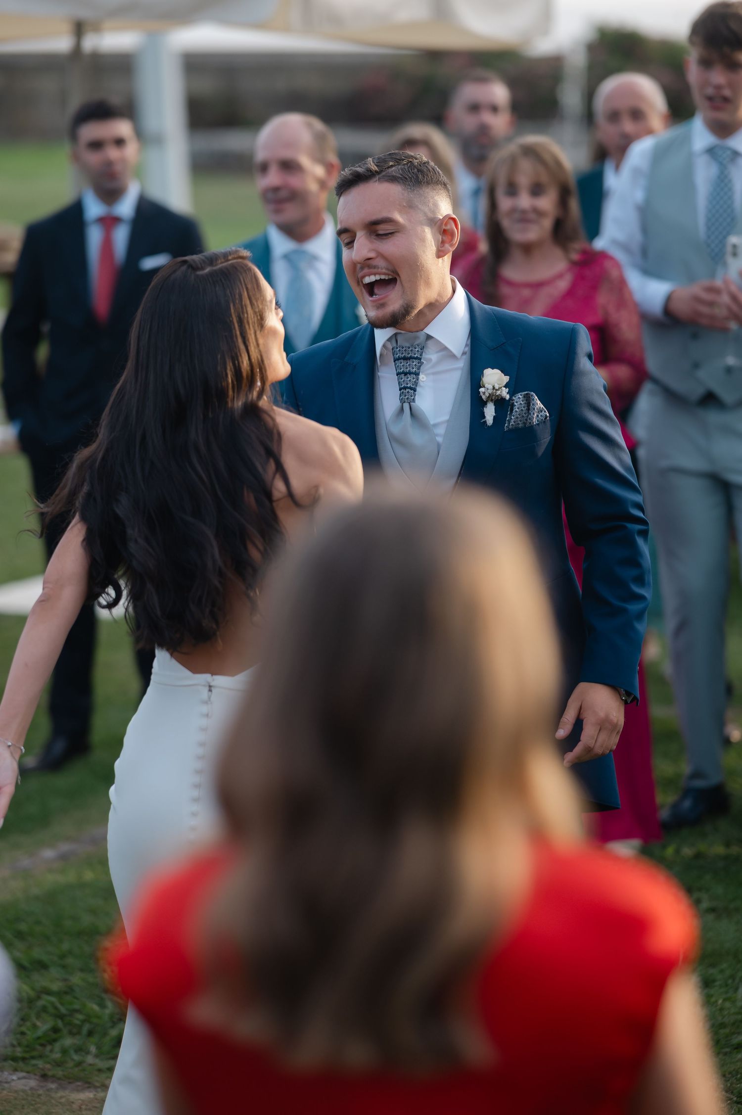 Wedding guests gather outdoors on a grassy lawn during a joyful celebration.