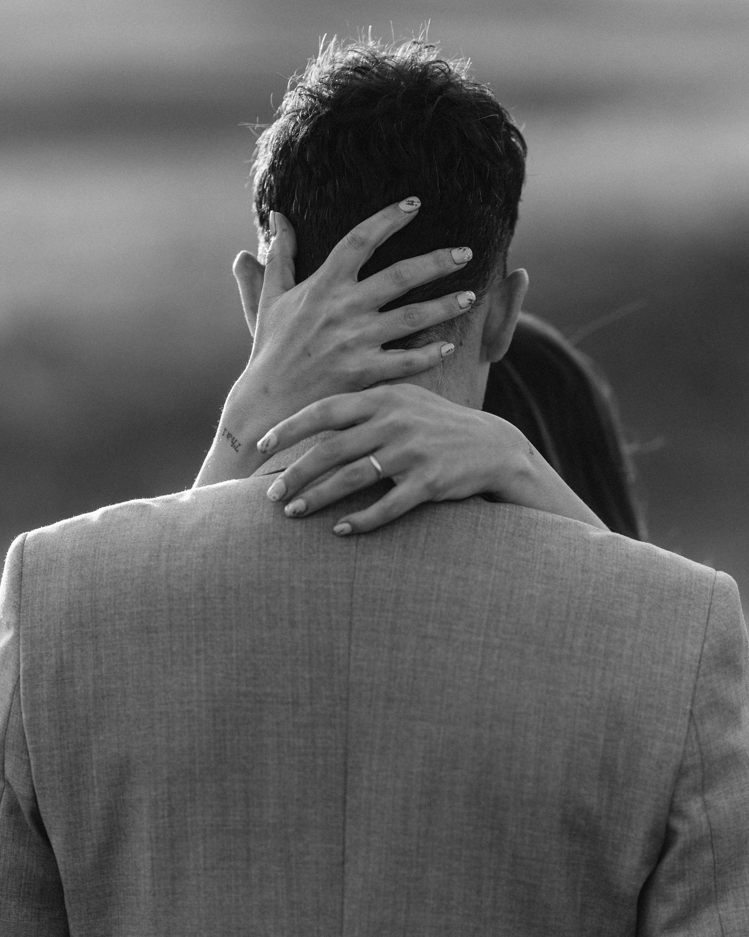 Black and white close-up of bride's hand with ring resting on groom's shoulder during wedding portrait.