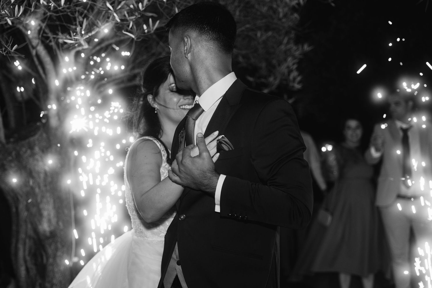 A black and white wedding photo collage shows romantic moments illuminated by sparklers during an evening celebration.