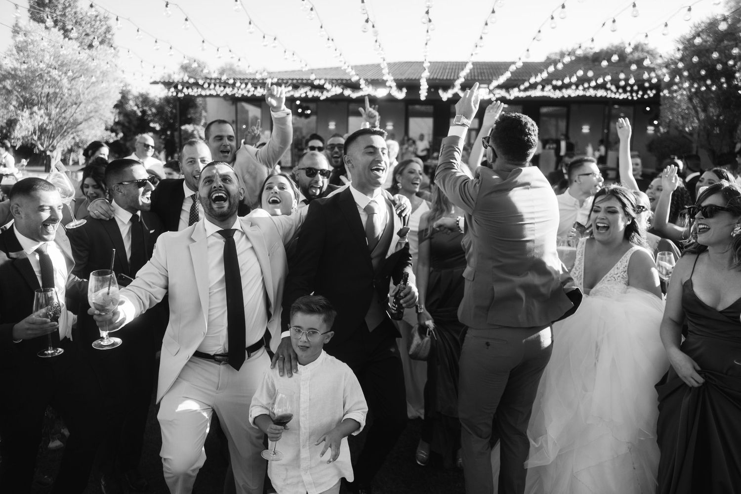 Black and white photo of wedding guests dancing and celebrating at an outdoor reception.