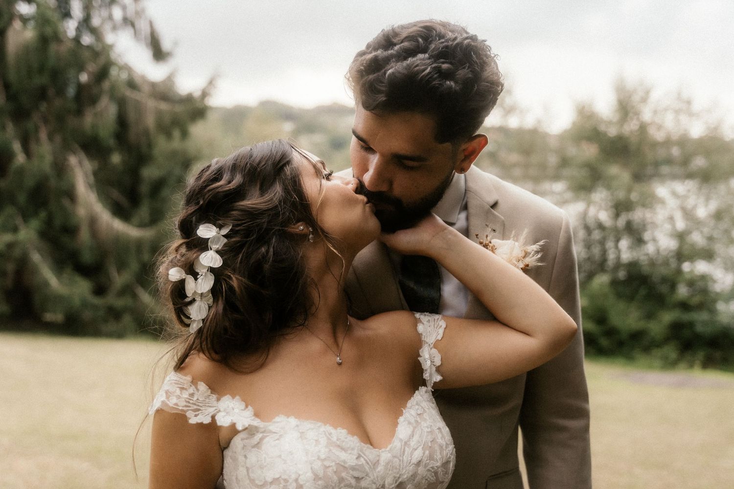 A romantic outdoor wedding photoshoot with a couple in formal attire embracing in a sunlit garden setting.