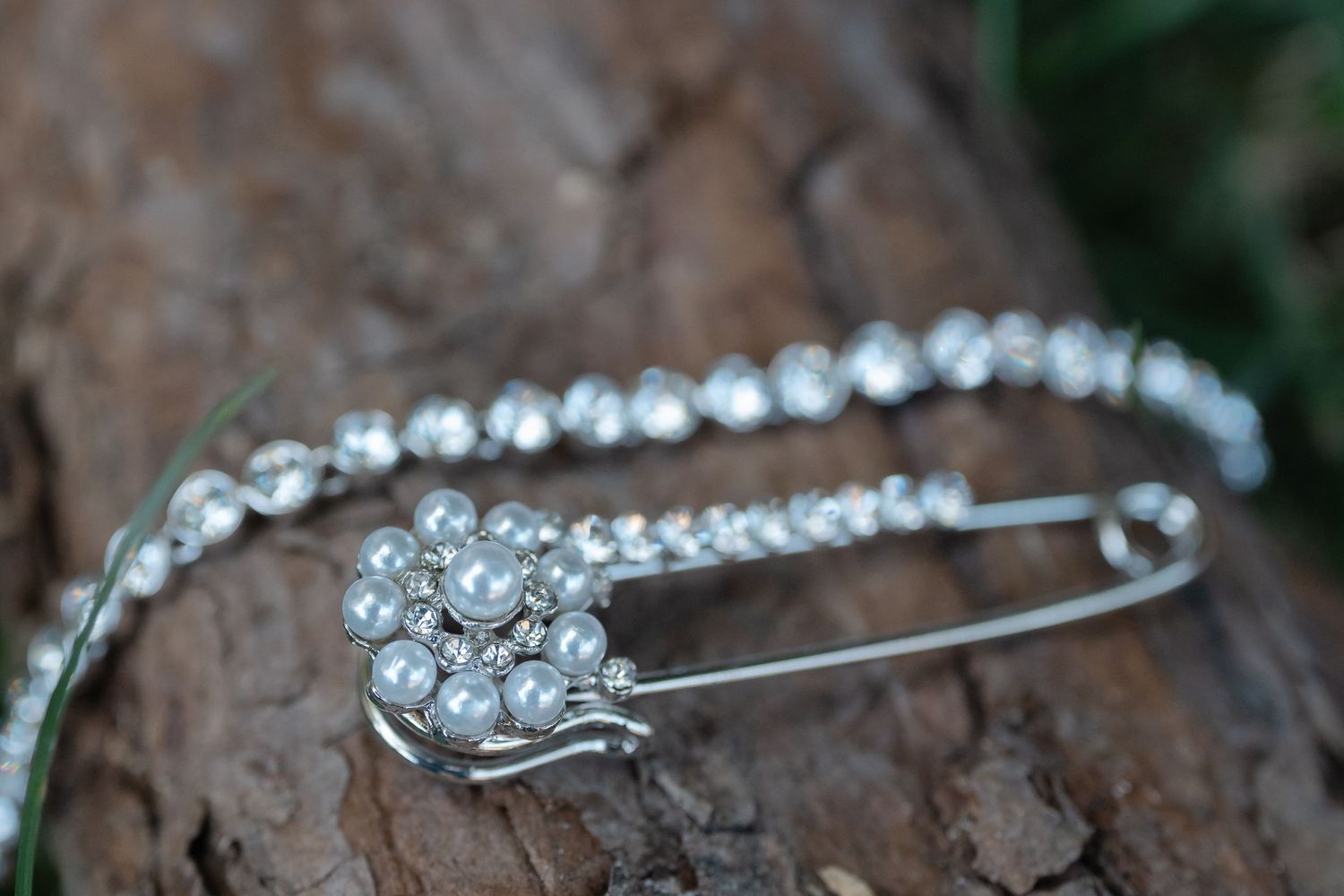 A delicate silver safety pin adorned with small crystal rhinestones rests against a textured wooden surface.