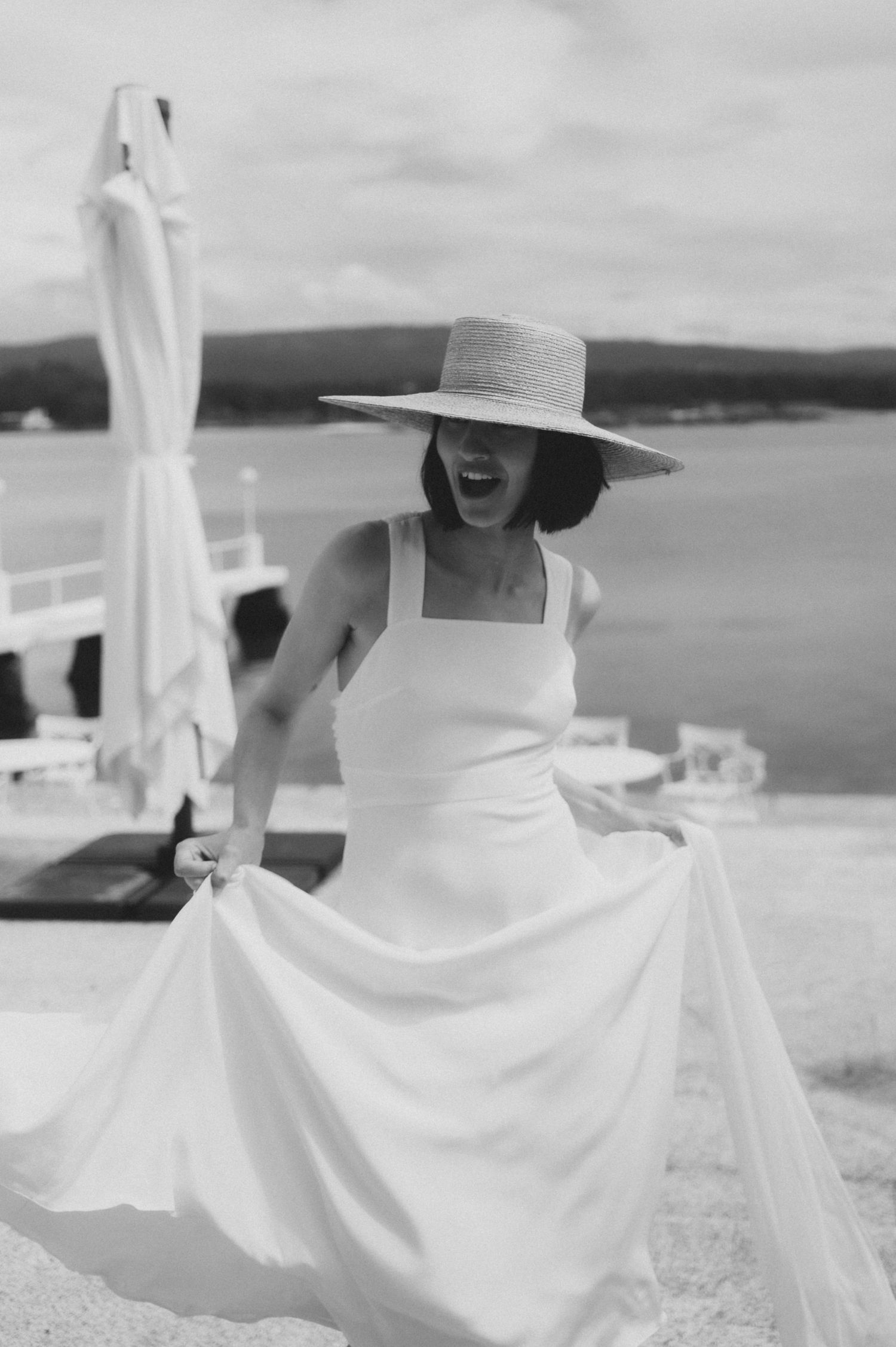 A dreamy black and white fashion photograph shows flowing white fabric against a coastal landscape backdrop.