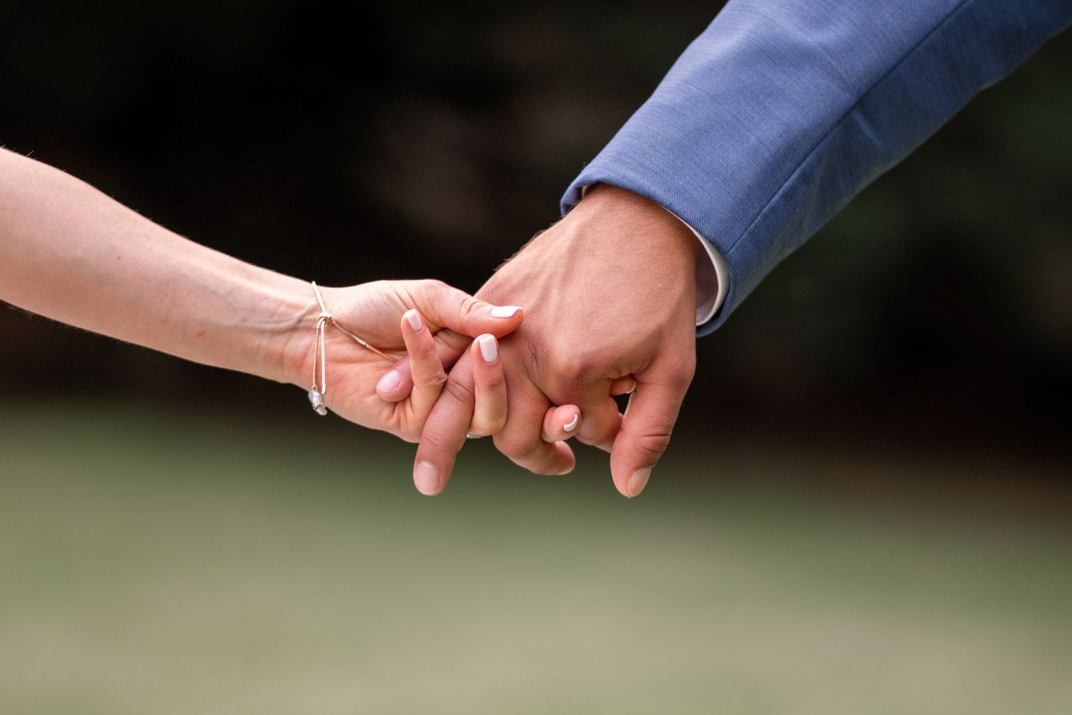 Close up of hands exchanging a gold wedding ring during an outdoor ceremony.