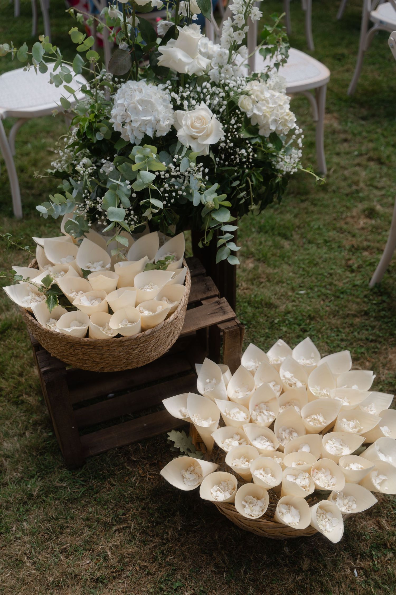 White paper cones filled with flower petals displayed in rustic wooden boxes and baskets with floral arrangements.