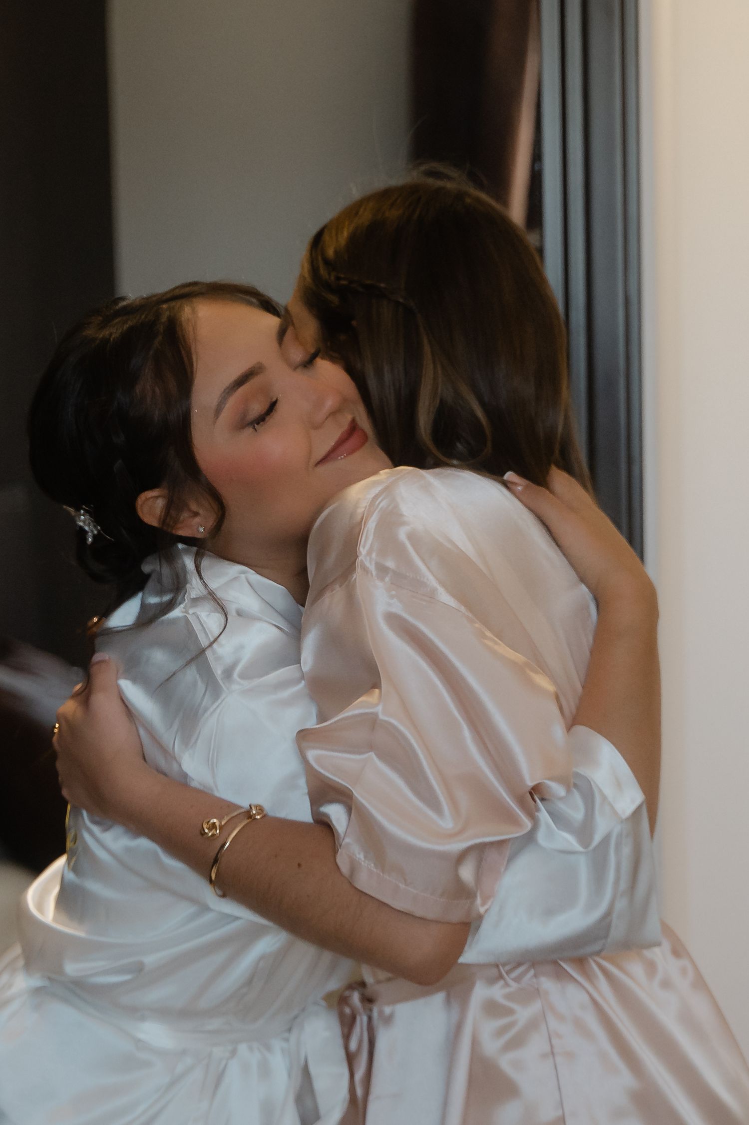 Two people embracing in white formal attire against a light background.