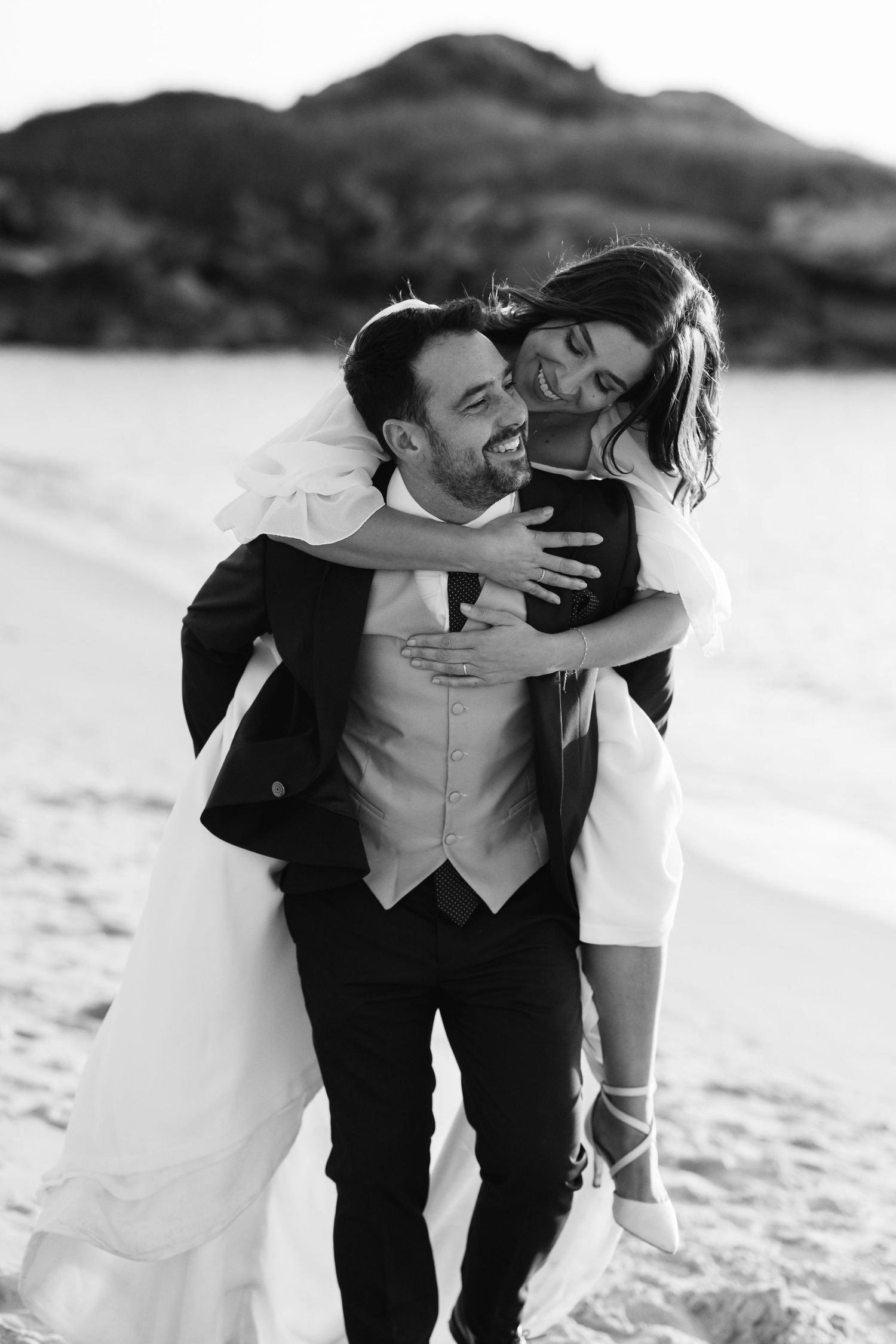 A happy couple shares intimate moments in black and white photos while walking together on a sandy beach.
