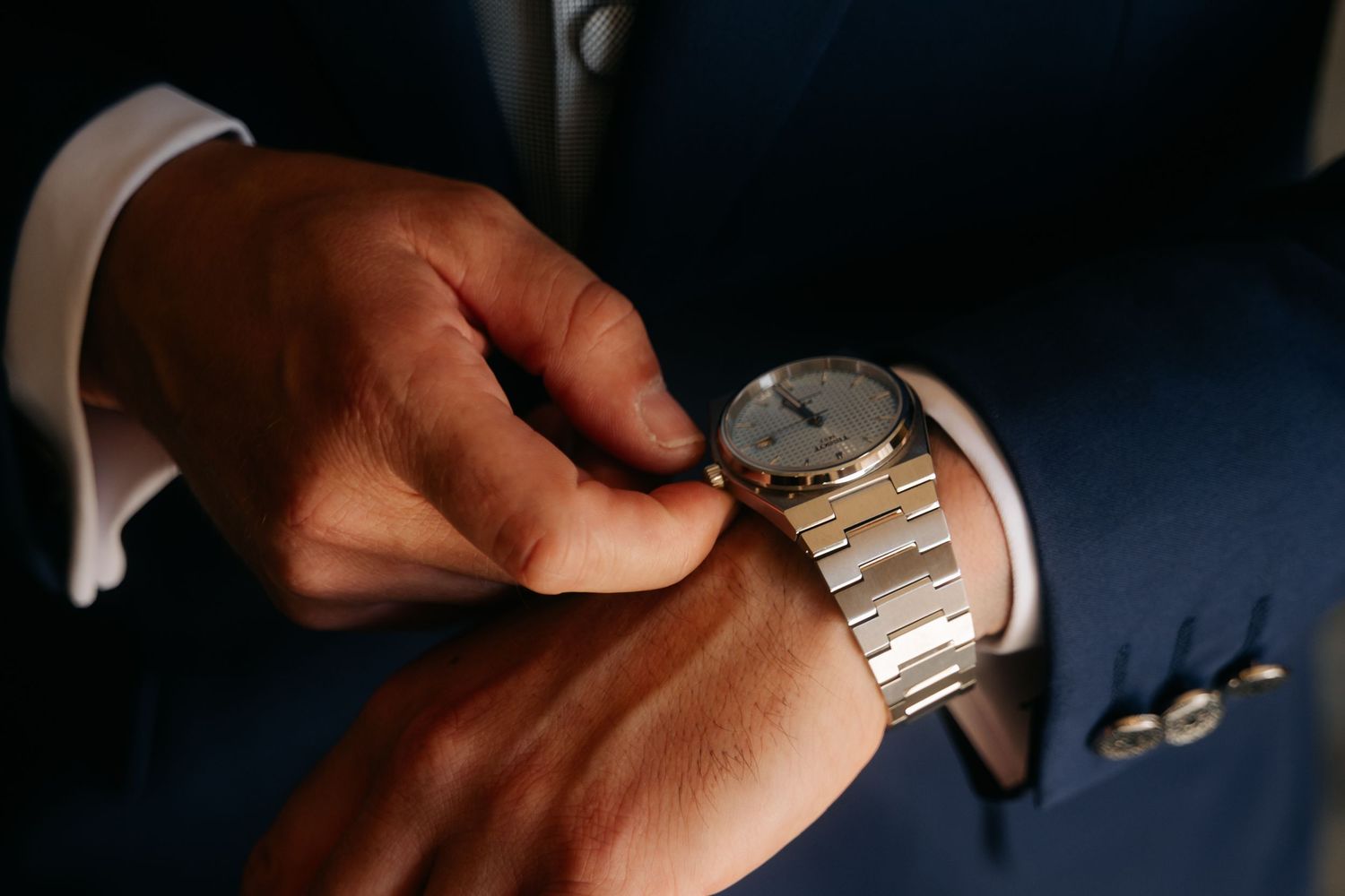Close-up of hands adjusting a silver wristwatch on a dark background.