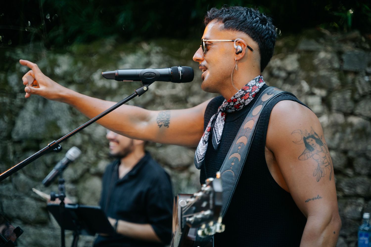 Musicians perform at an outdoor concert venue against a stone wall backdrop during sunset.