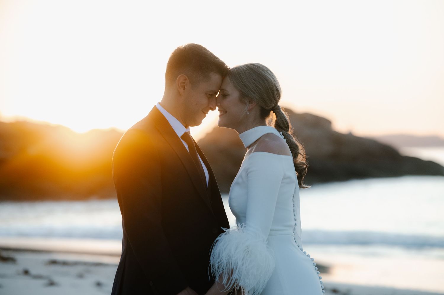 Sunset silhouette of wedding couple sharing intimate moment by the ocean.