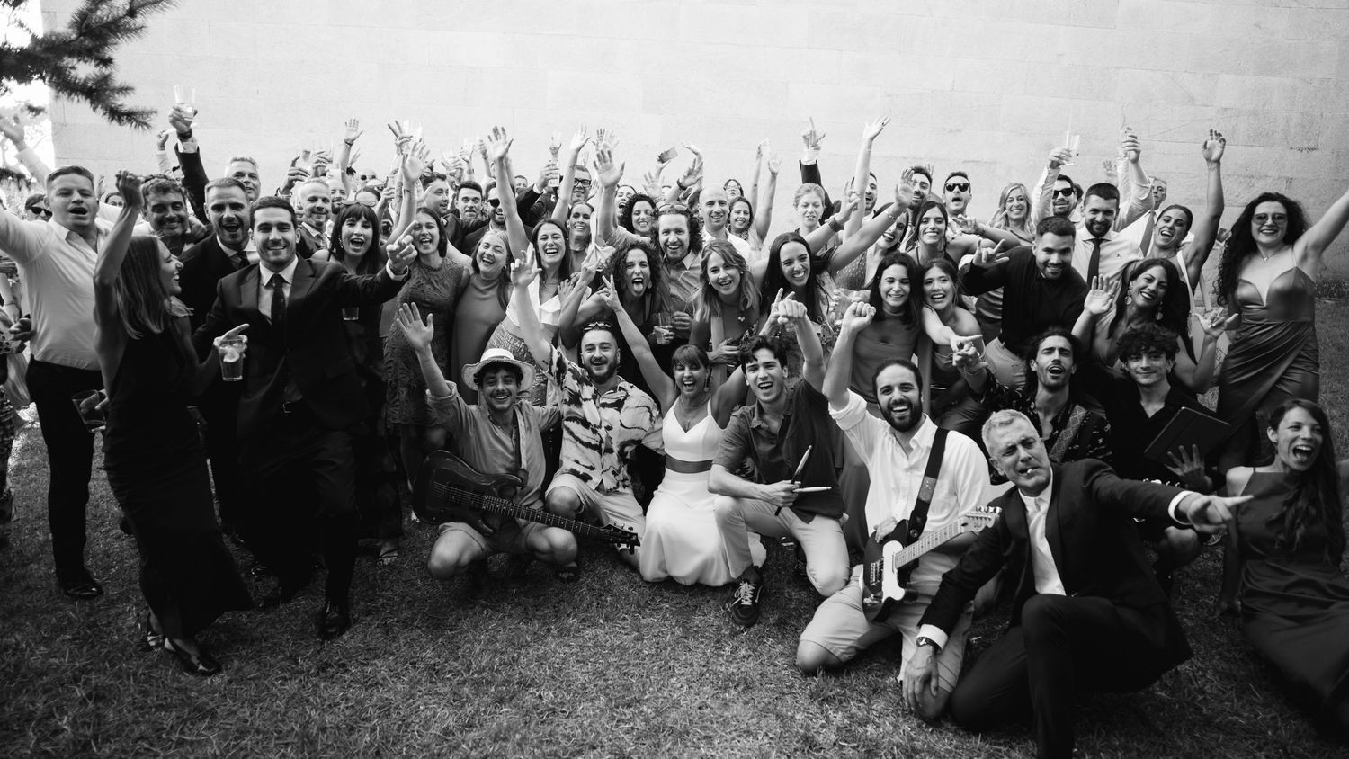Large group of wedding guests pose together for a celebratory black and white photo on a lawn.