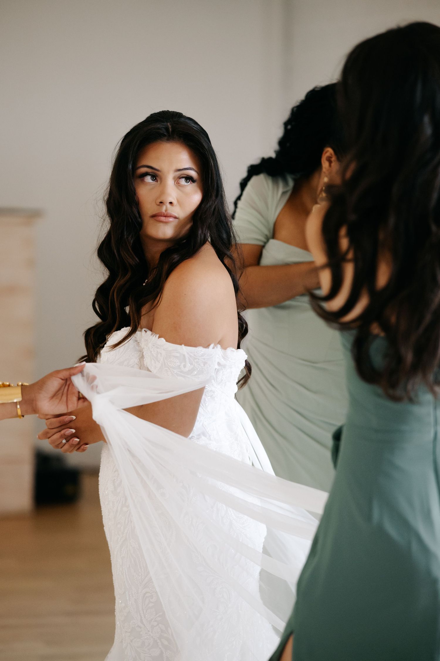 A bride getting help putting on her elegant white off-shoulder wedding dress during preparation.