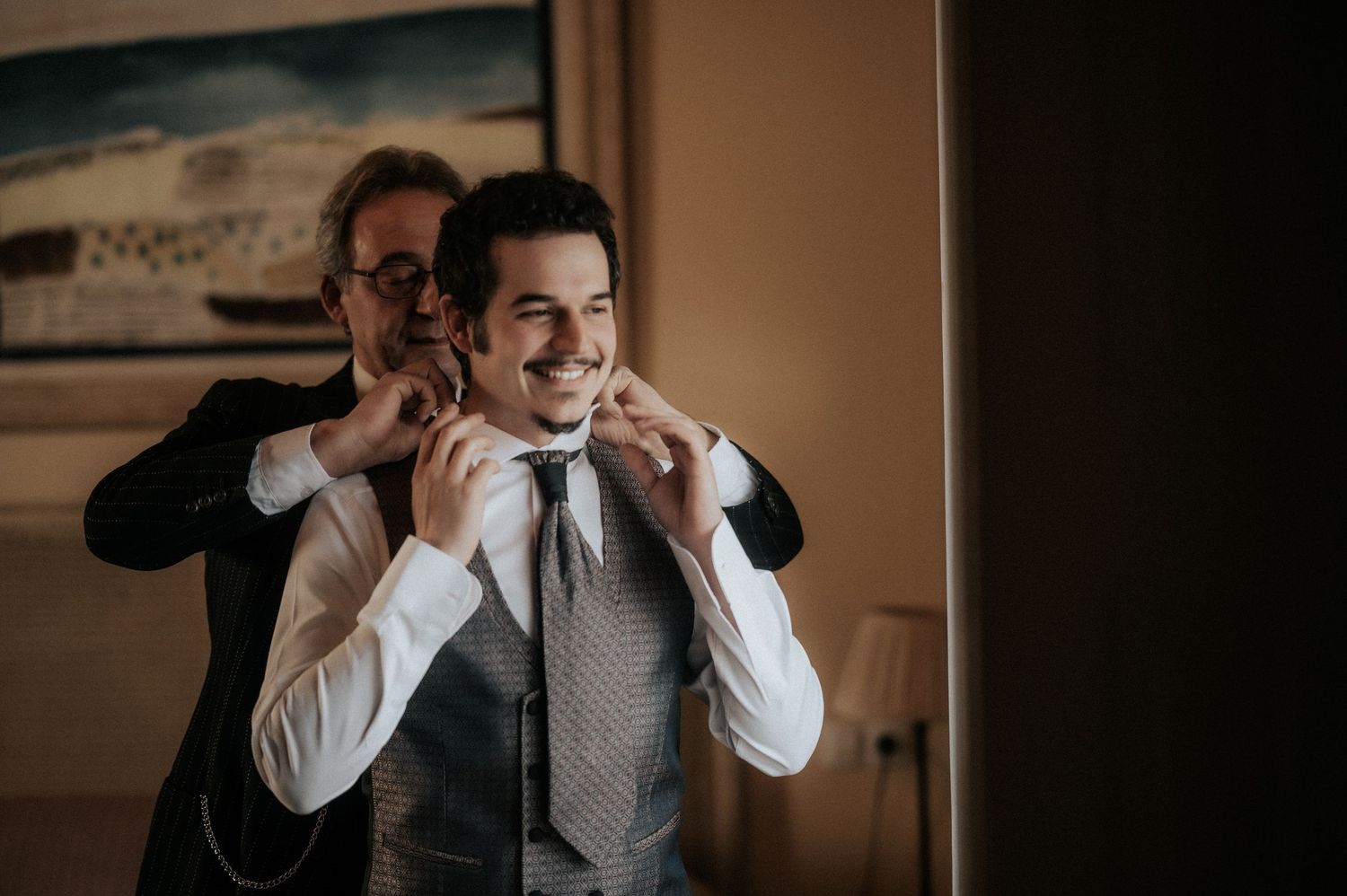 A sequence of images showing someone in a gray suit vest adjusting a white tie in warm indoor lighting.