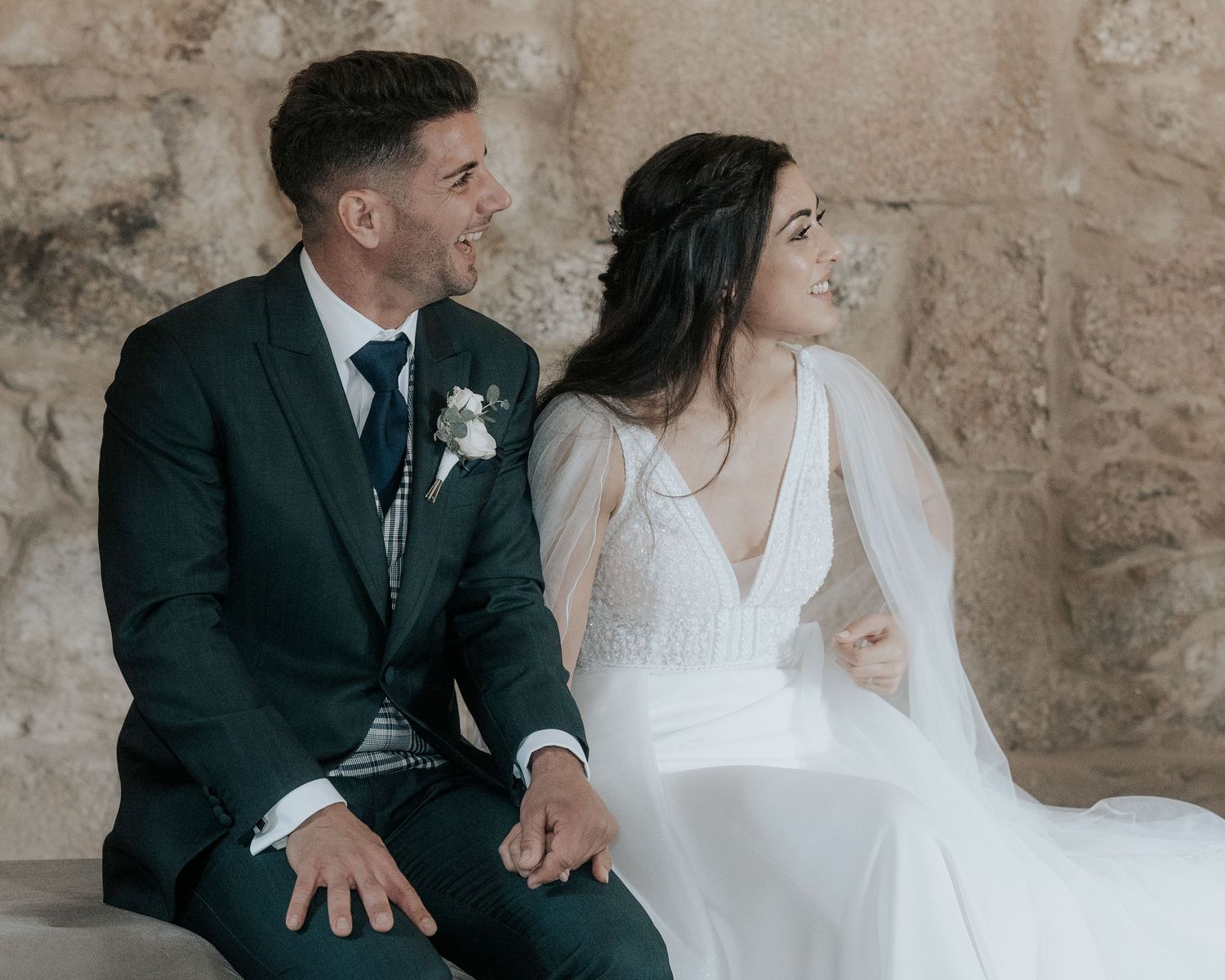 Couple shares intimate moments during their wedding ceremony against a rustic stone wall backdrop.