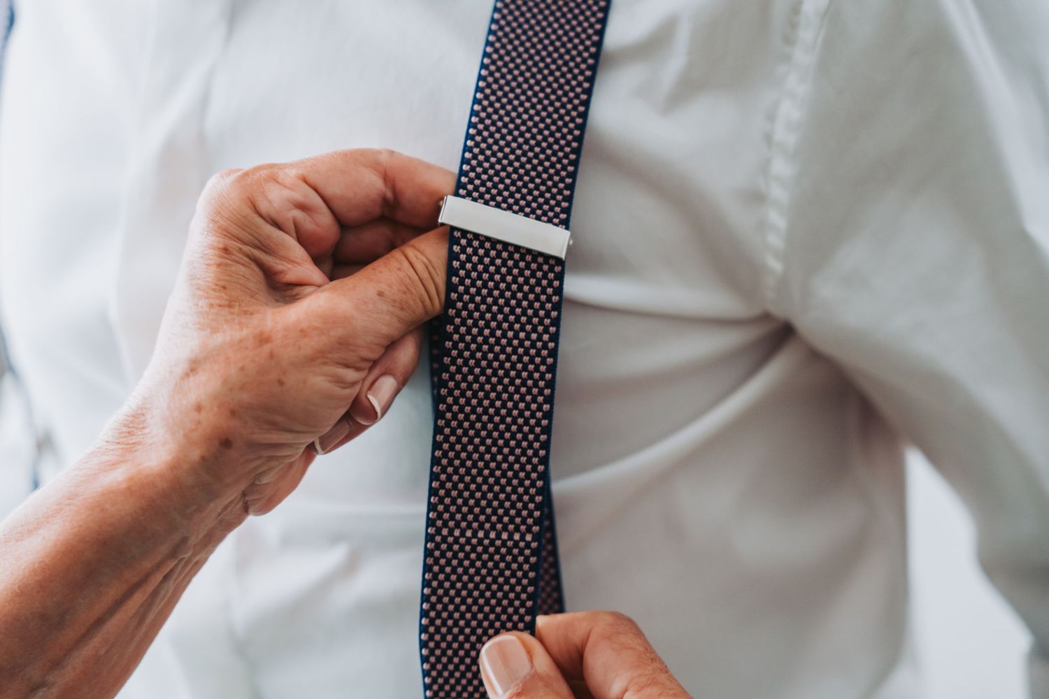 A close-up series showing hands adjusting a navy polka dot necktie against a white dress shirt.