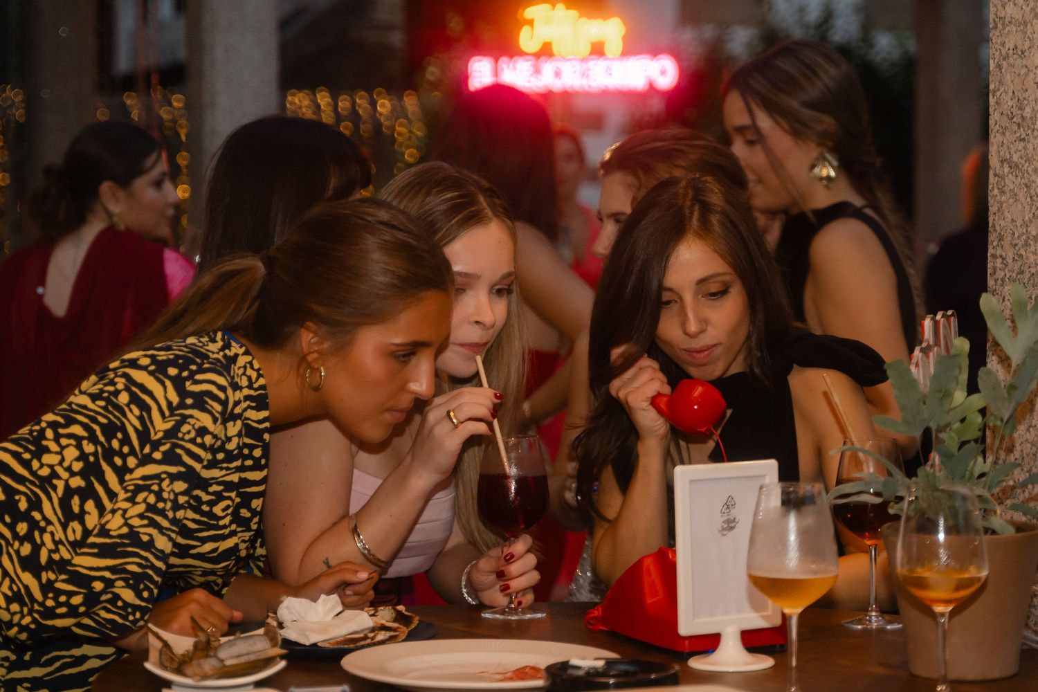 Wedding reception guests enjoying dinner and drinks at tables illuminated by warm lighting.