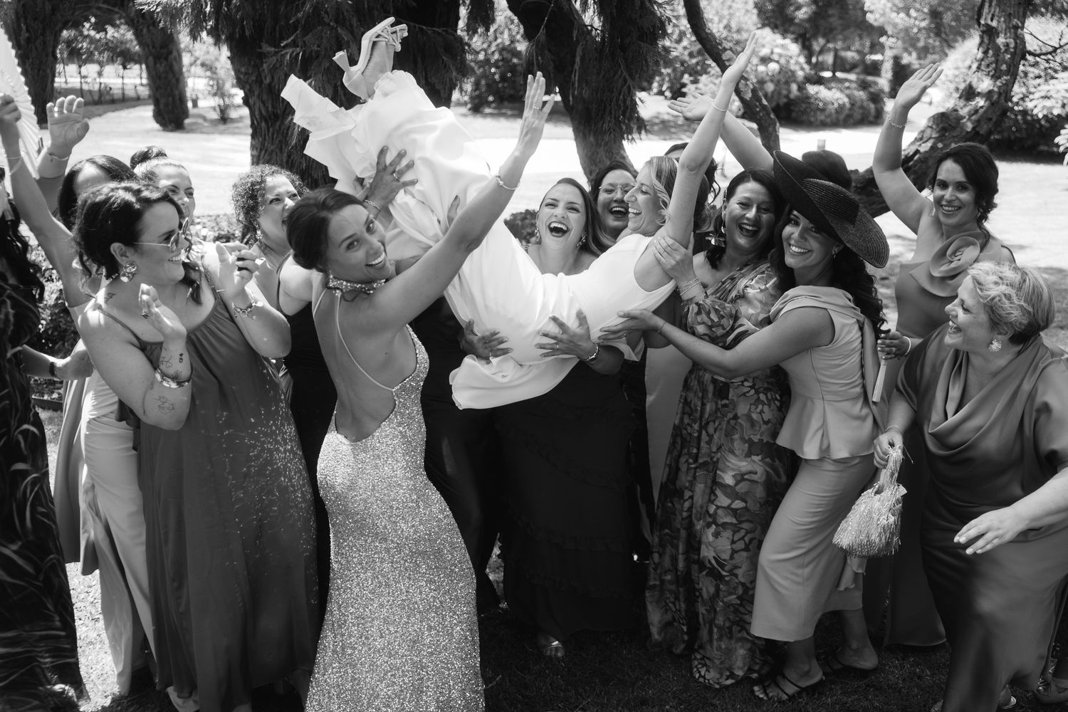 Black and white photo of wedding guests dancing and celebrating with arms raised.