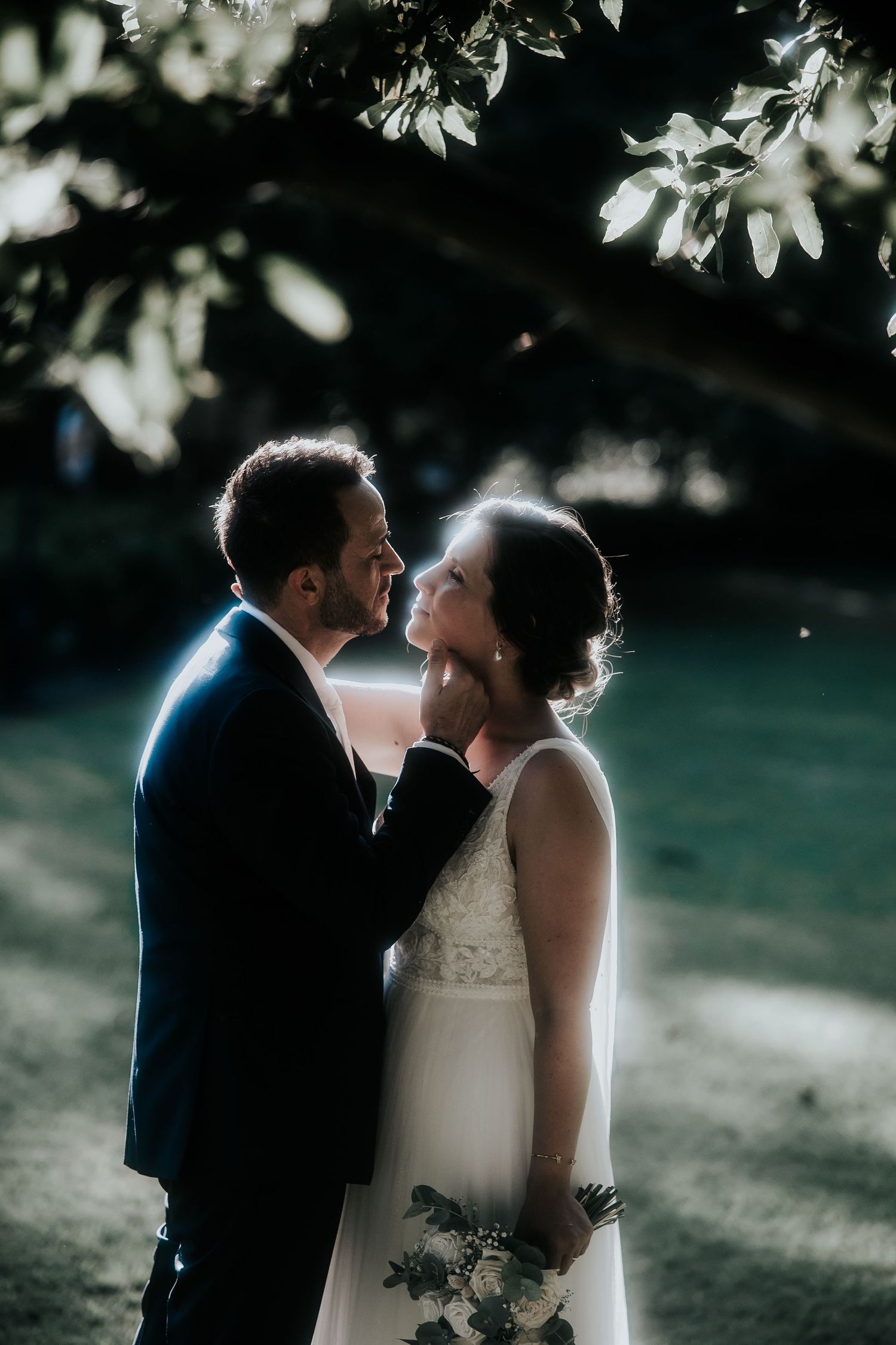 A romantic wedding couple shares an intimate moment in a sunlit garden with soft backlighting and dreamy atmosphere.
