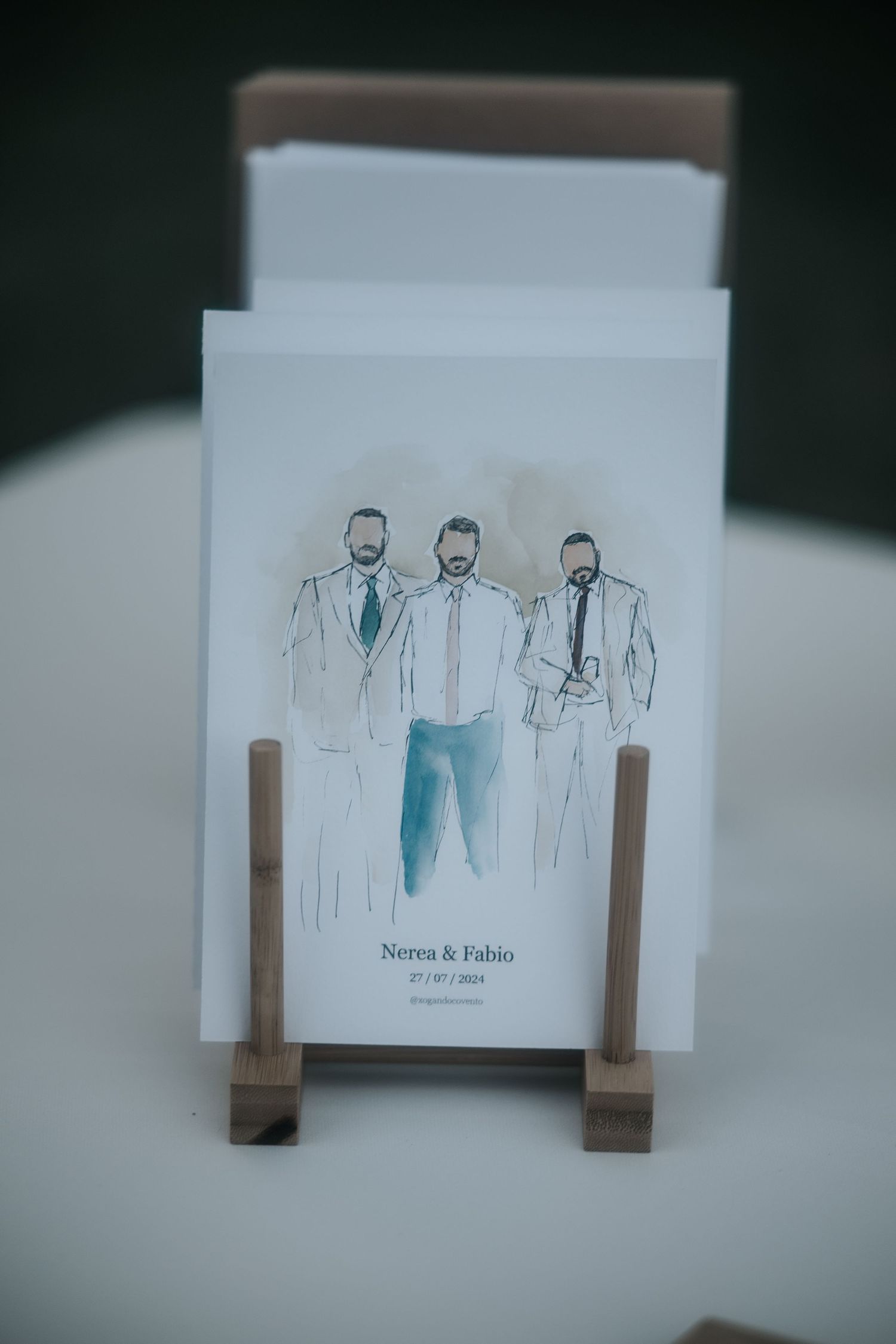 Minimalist watercolor wedding invitation cards displayed with simple wooden holders on a white surface.