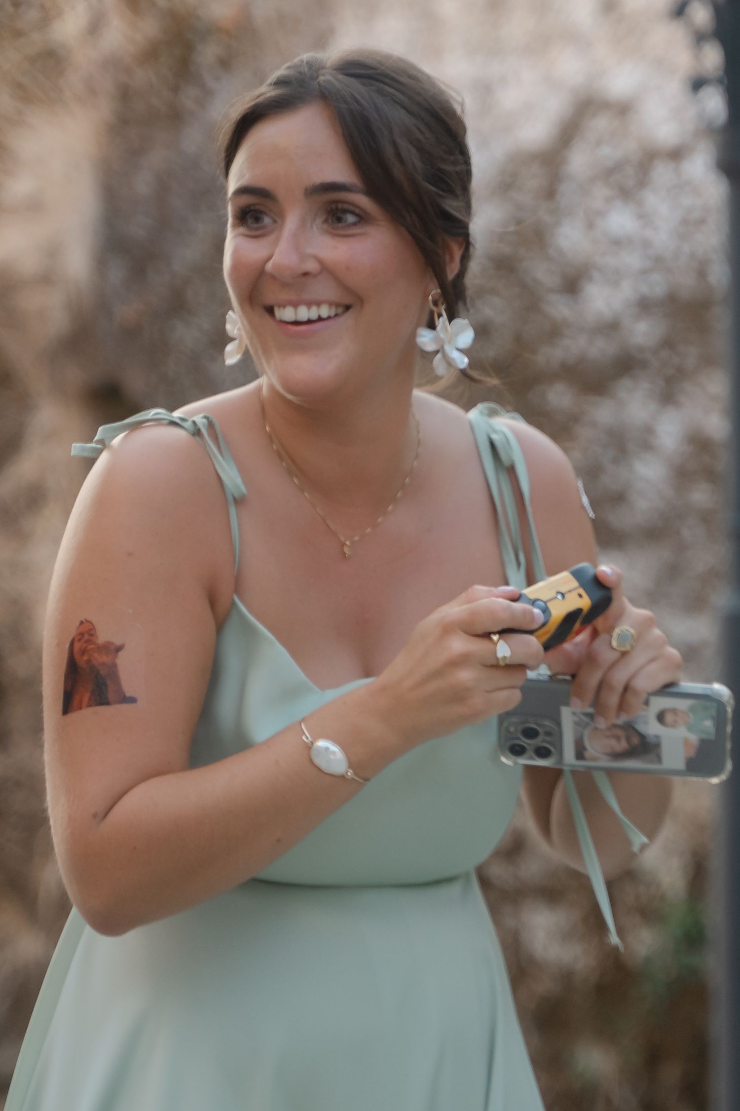 A bridesmaid in a mint green dress laughs while holding drinks at an outdoor wedding reception.