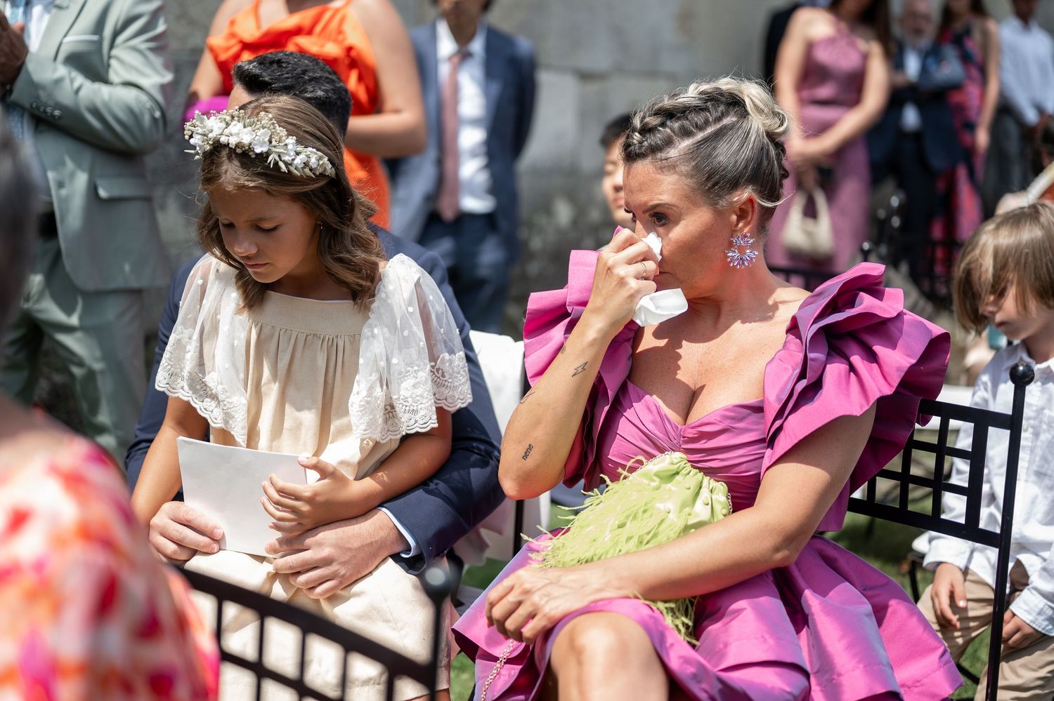 A group of people sitting on a bench in colorful dresses and formal attire at an outdoor event.