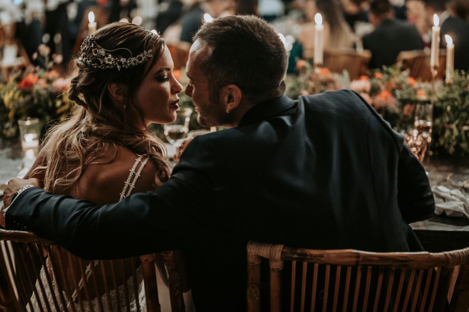 Wedding guests enjoy a candlelit dinner reception at rustic wooden tables in an intimate indoor venue.