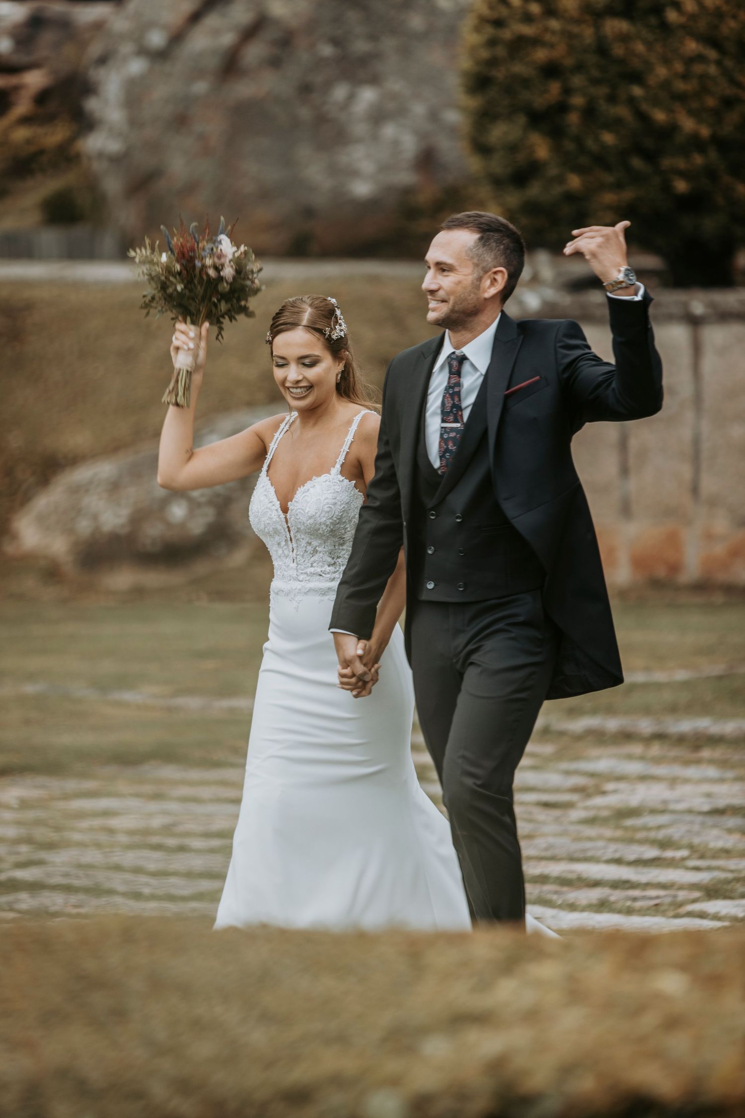 A newlywed couple dances and celebrates joyfully together on stone pavement during an outdoor wedding celebration.