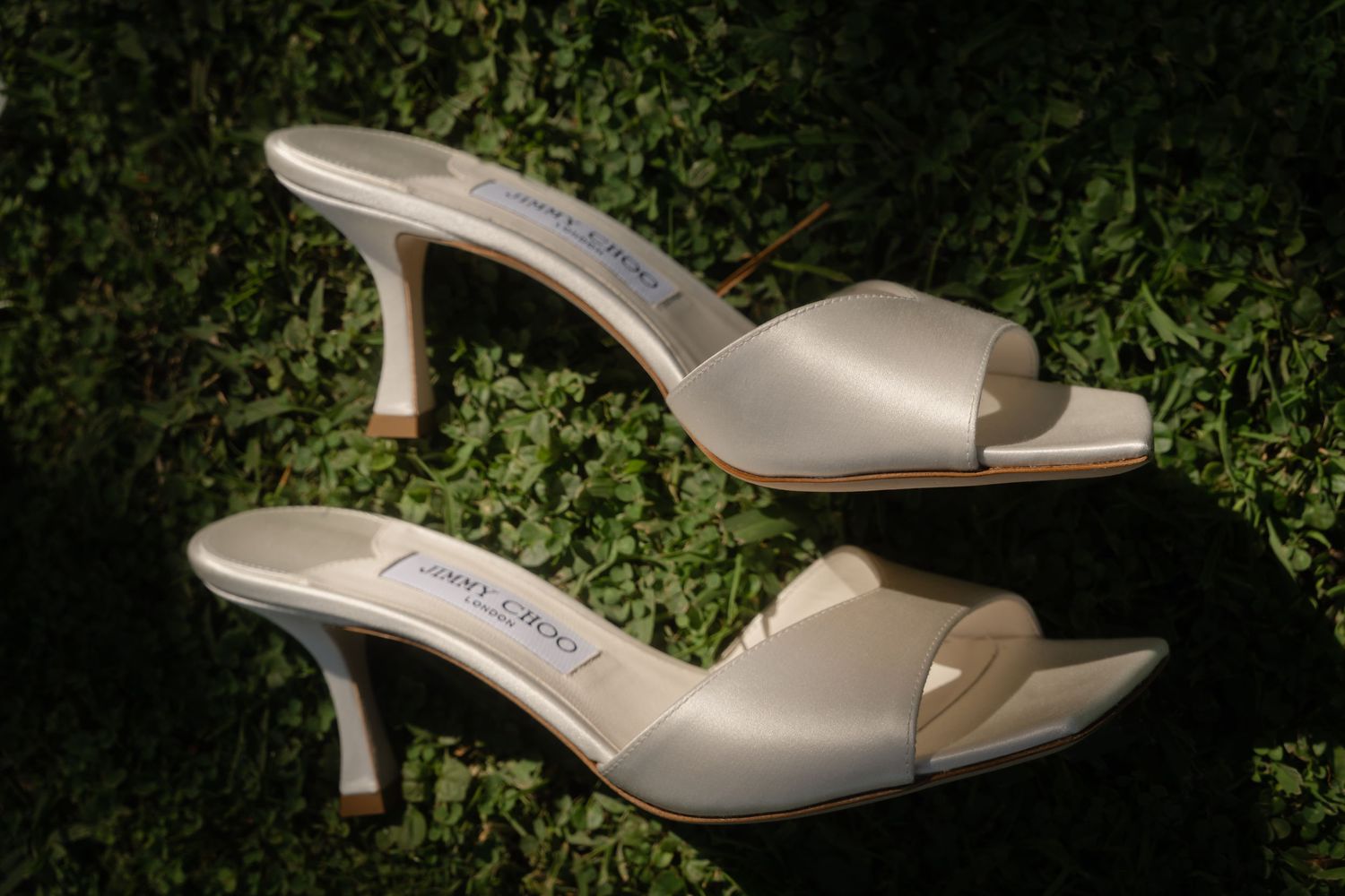 Elegant ivory satin bridal heels with kitten heel displayed on green foliage background.