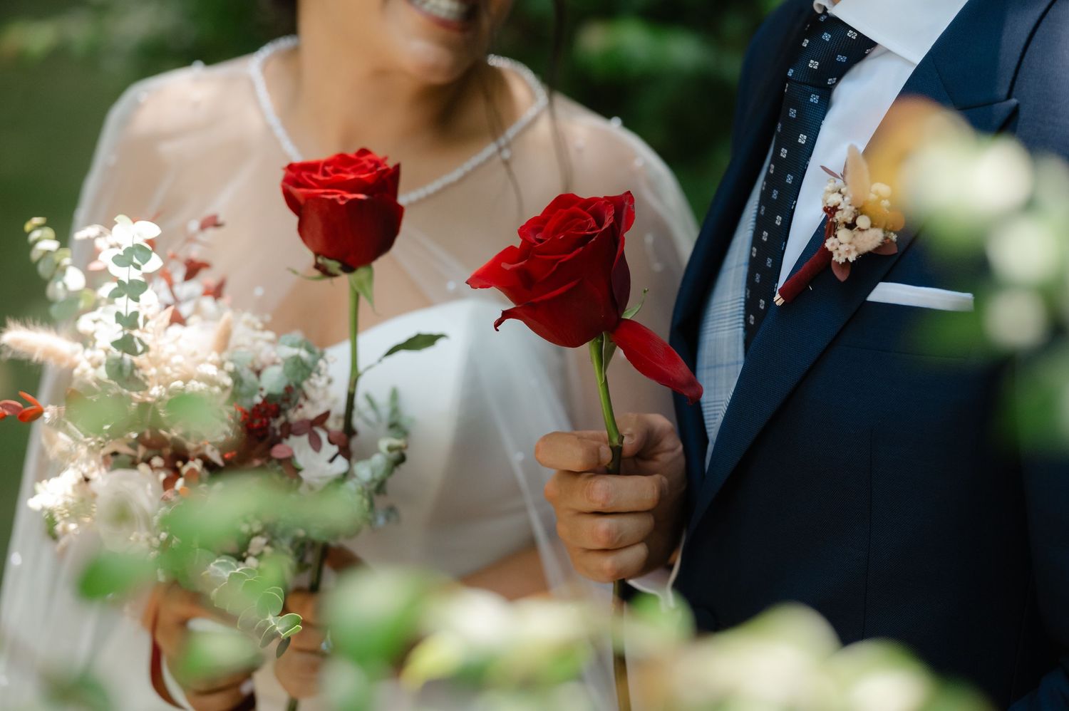 Wedding party members hold vibrant red roses against a soft blurred outdoor background during a ceremony.