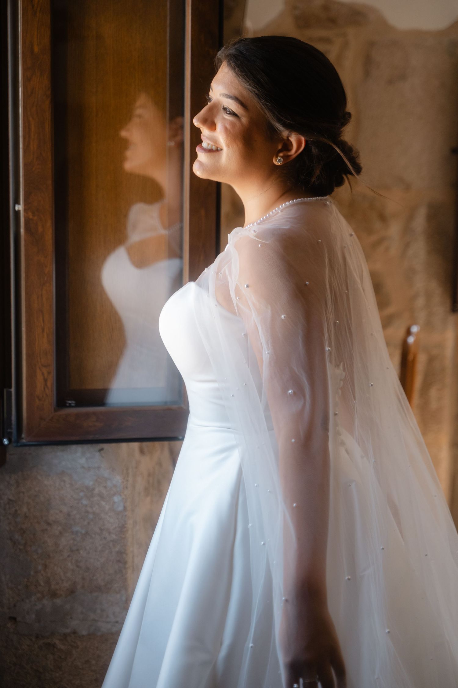 Elegant white wedding dress with flowing veil captured in soft window light.
