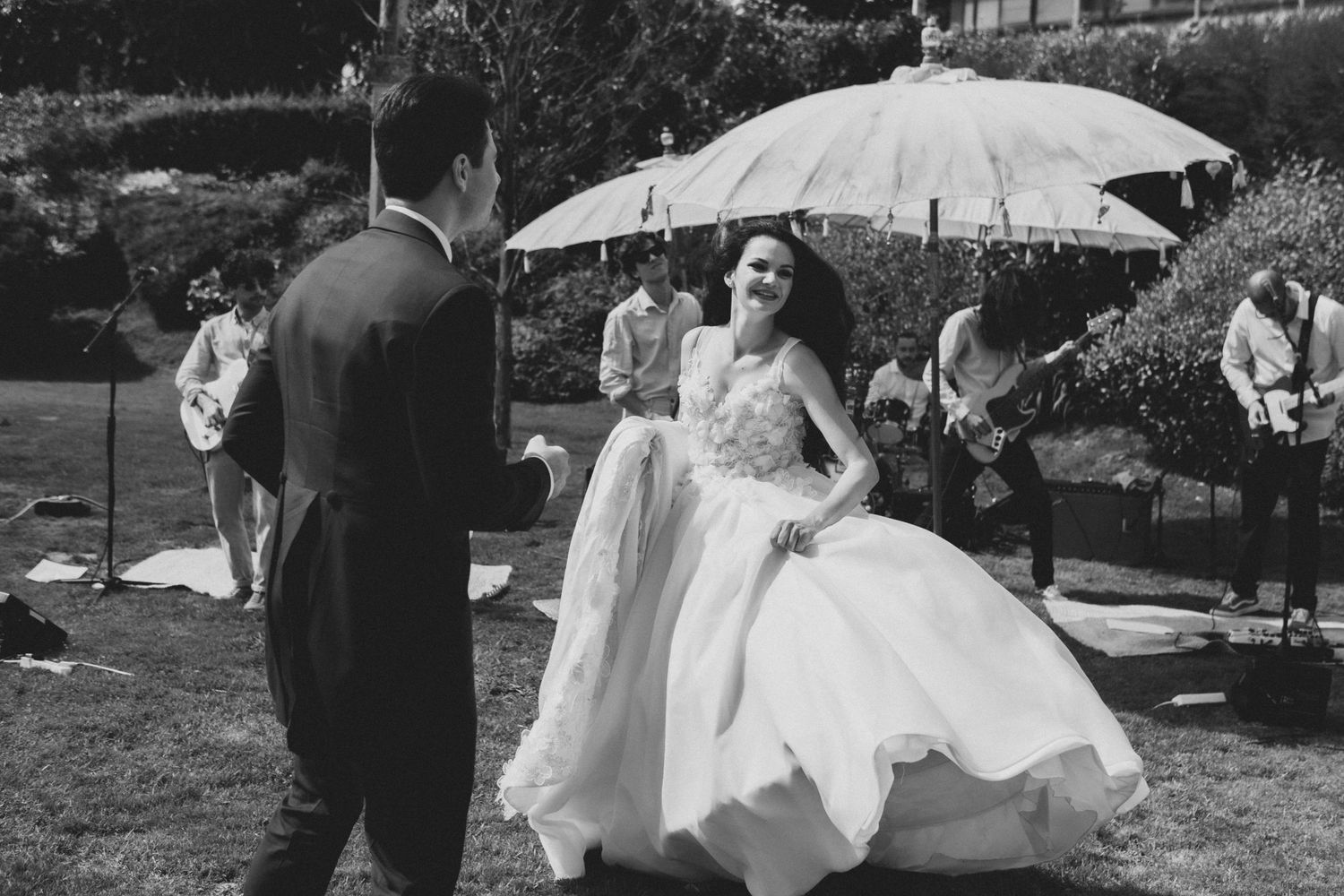 Wedding couple shares playful moments outdoors under a white parasol in a garden setting.