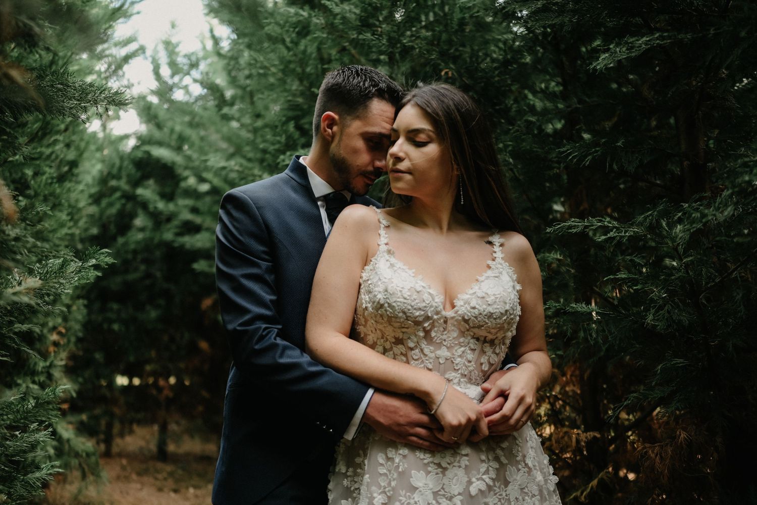 A romantic couple embraces in a lush forest setting during their wedding photoshoot.