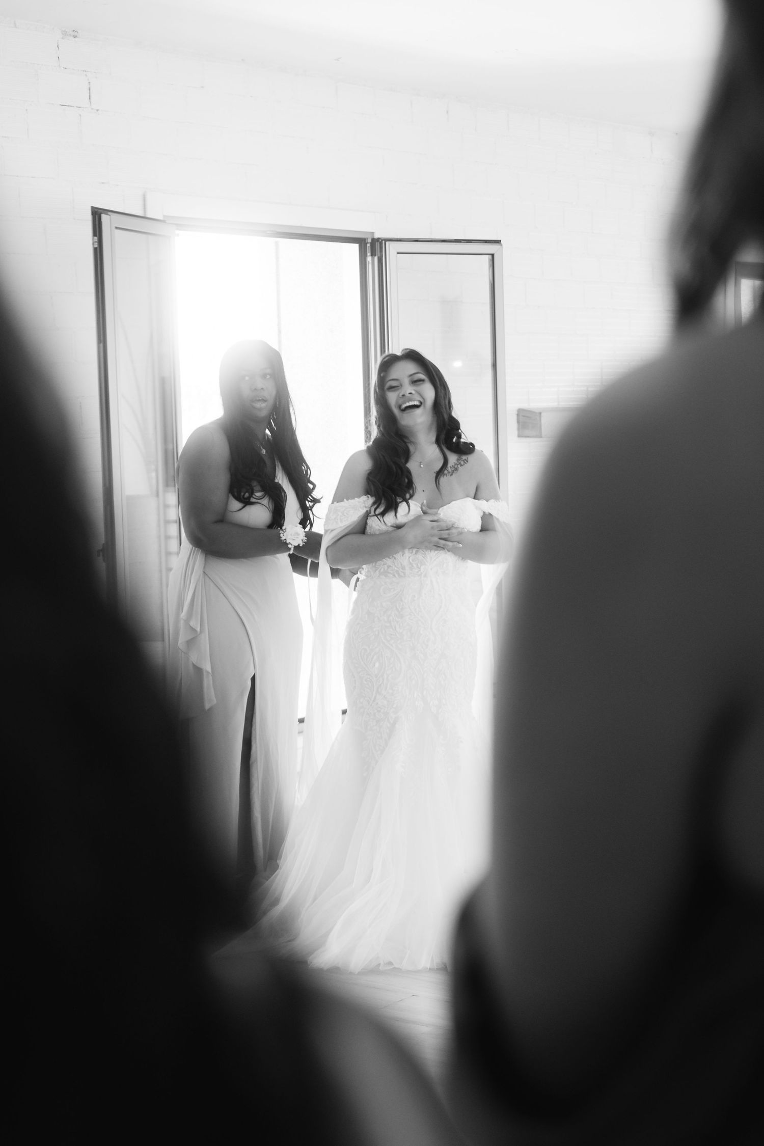 Sunlit black and white candid moment showing joyful wedding day preparations in a bright room.