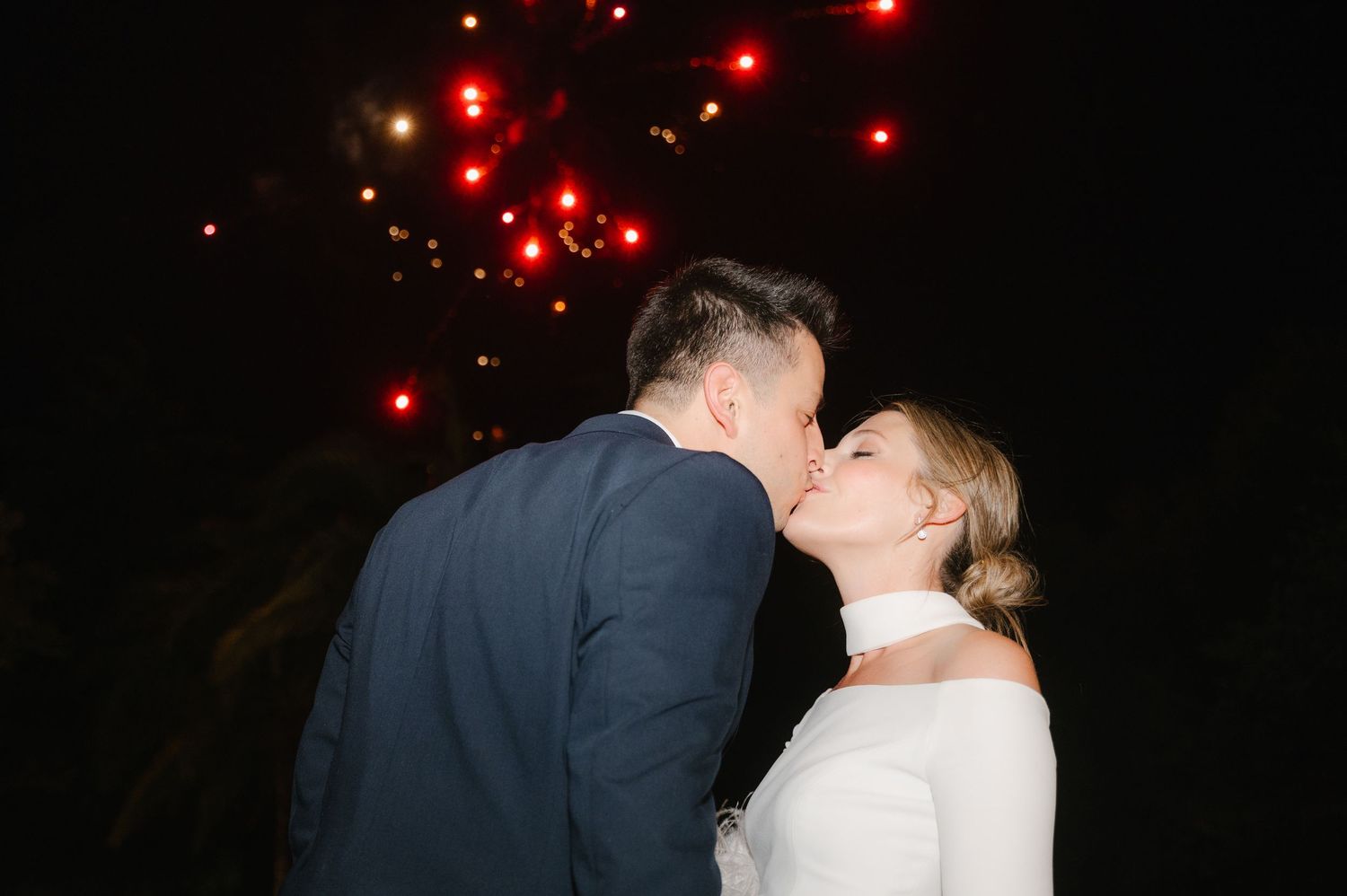 A romantic silhouette of a couple kissing at night with red lights glowing in the background.