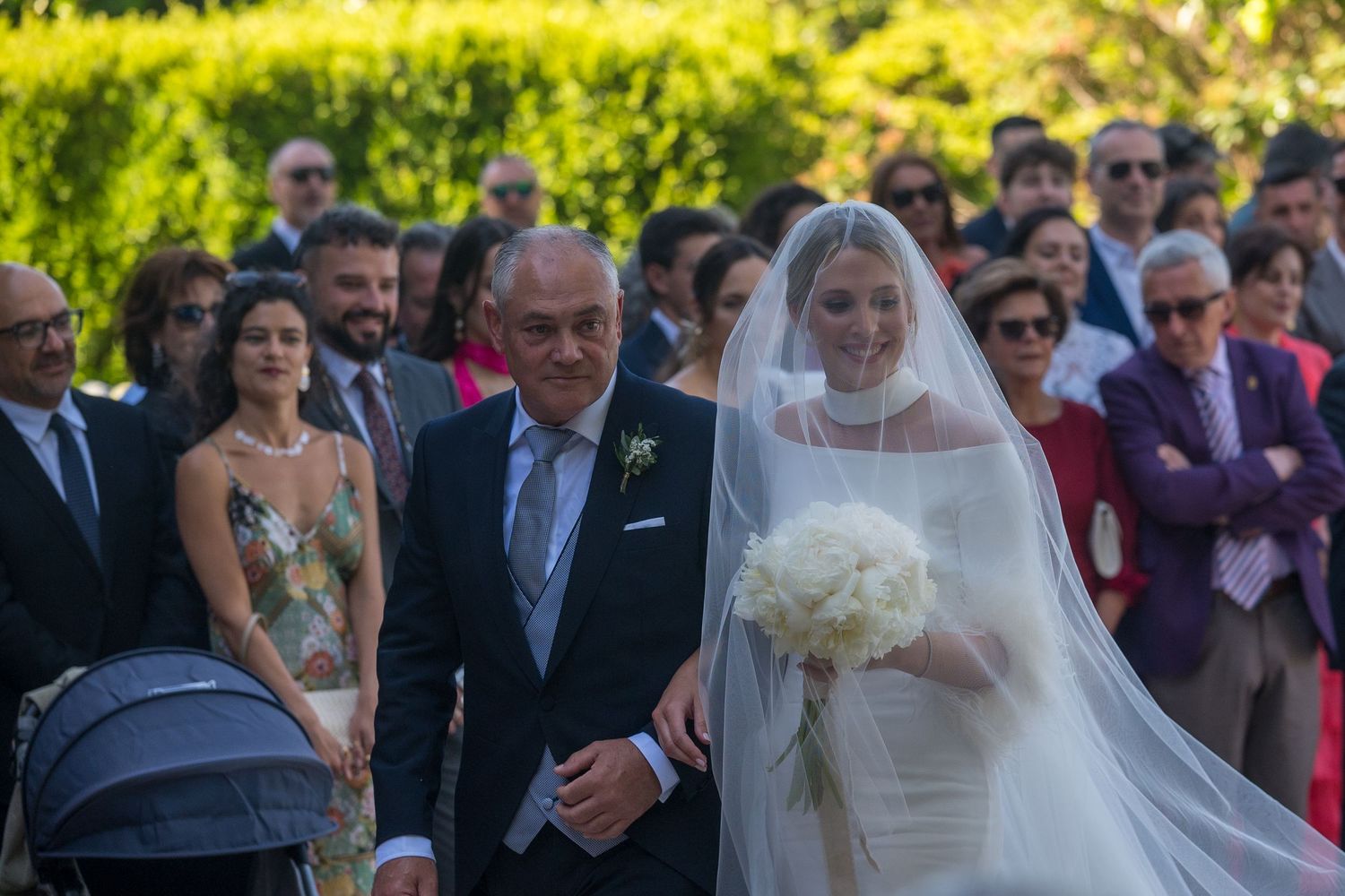 Wedding guests gather outdoors in a sunny garden setting during a joyful celebration ceremony.